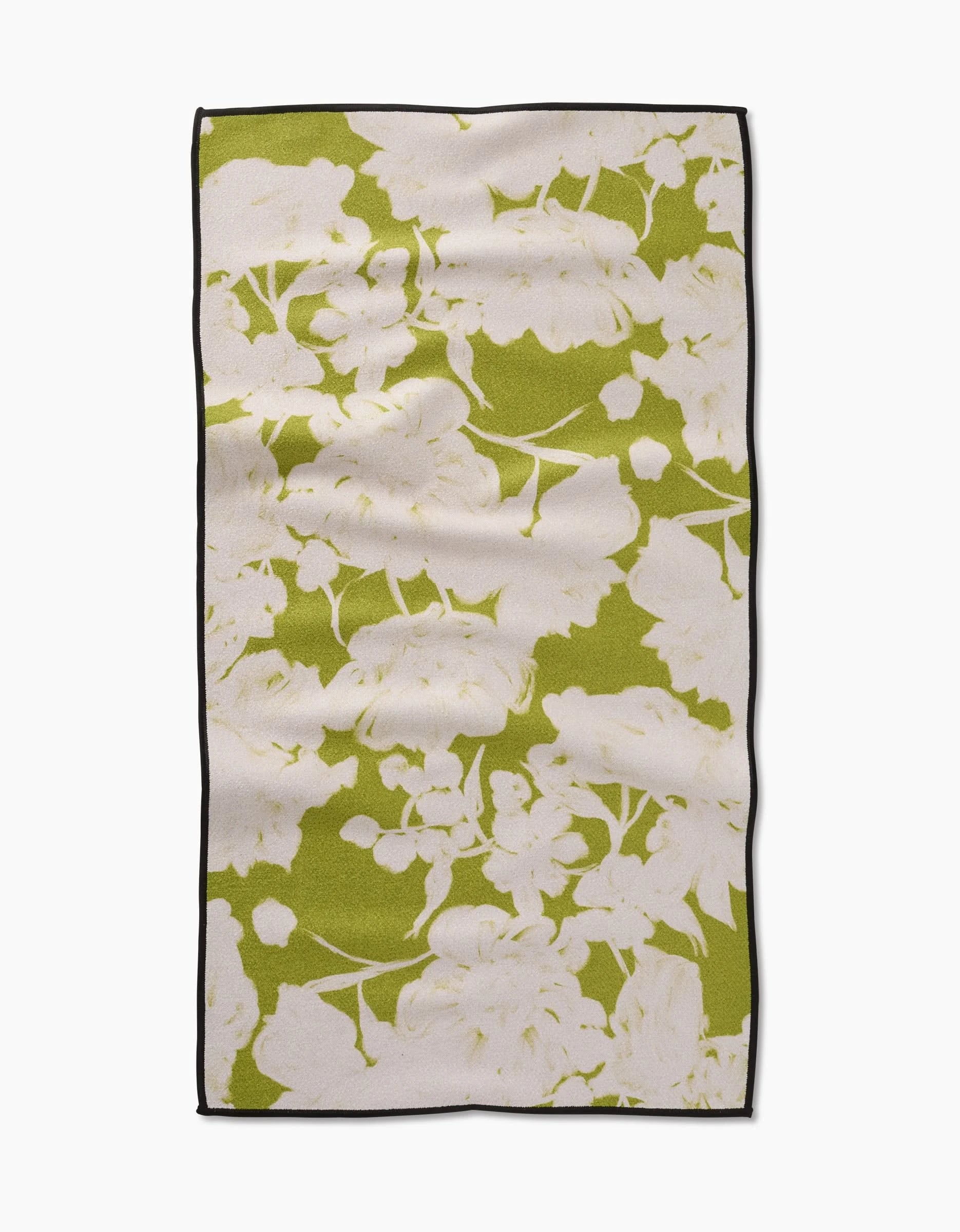The GEOMETRY Meadow Mist fitness towel, made from ultra-absorbent recycled materials, showcases a white floral pattern on a green background with a black border and is displayed on a plain white surface.