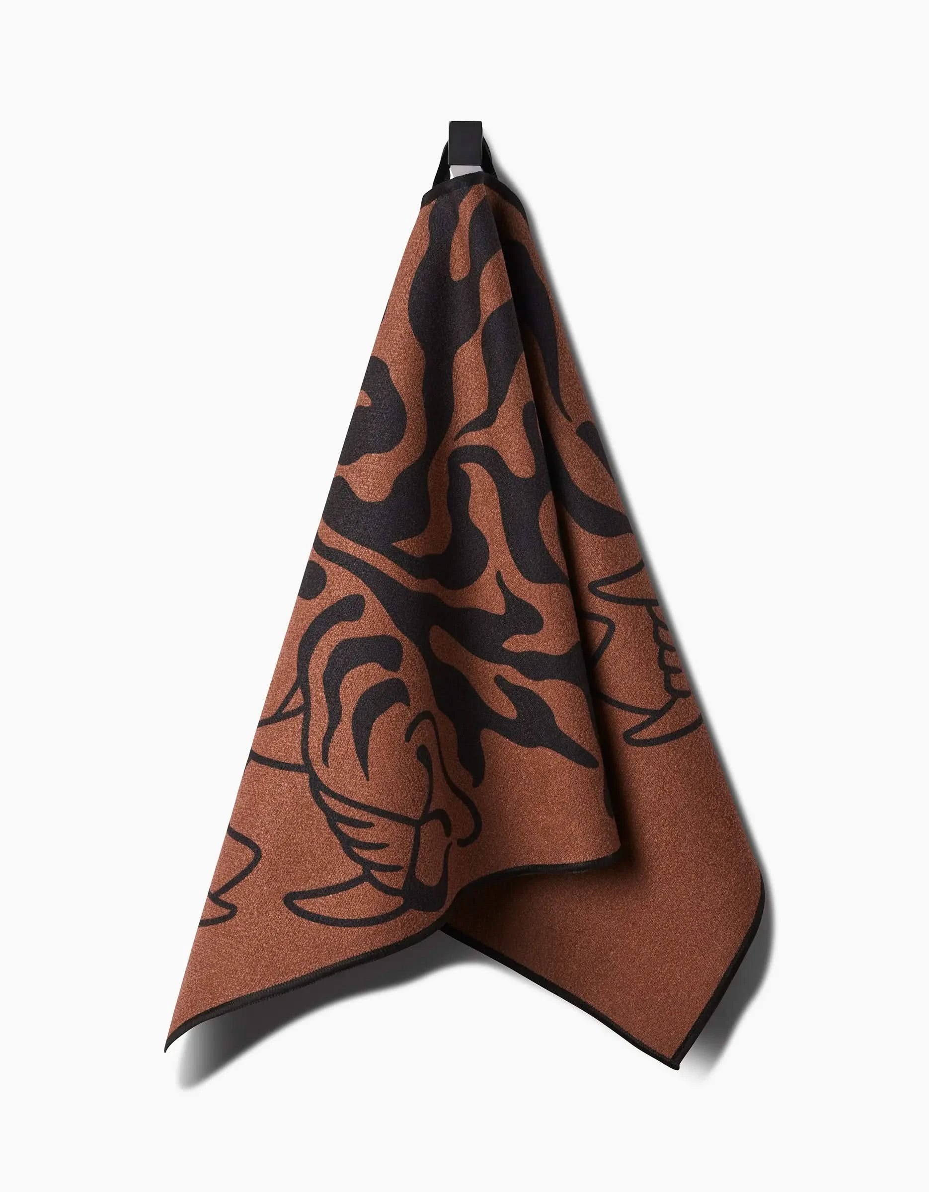 The Cole Strem “Panther In Brown” towel, ultra-absorbent with a bold abstract panther face in brown and black, hangs from a black loop against a plain white background.