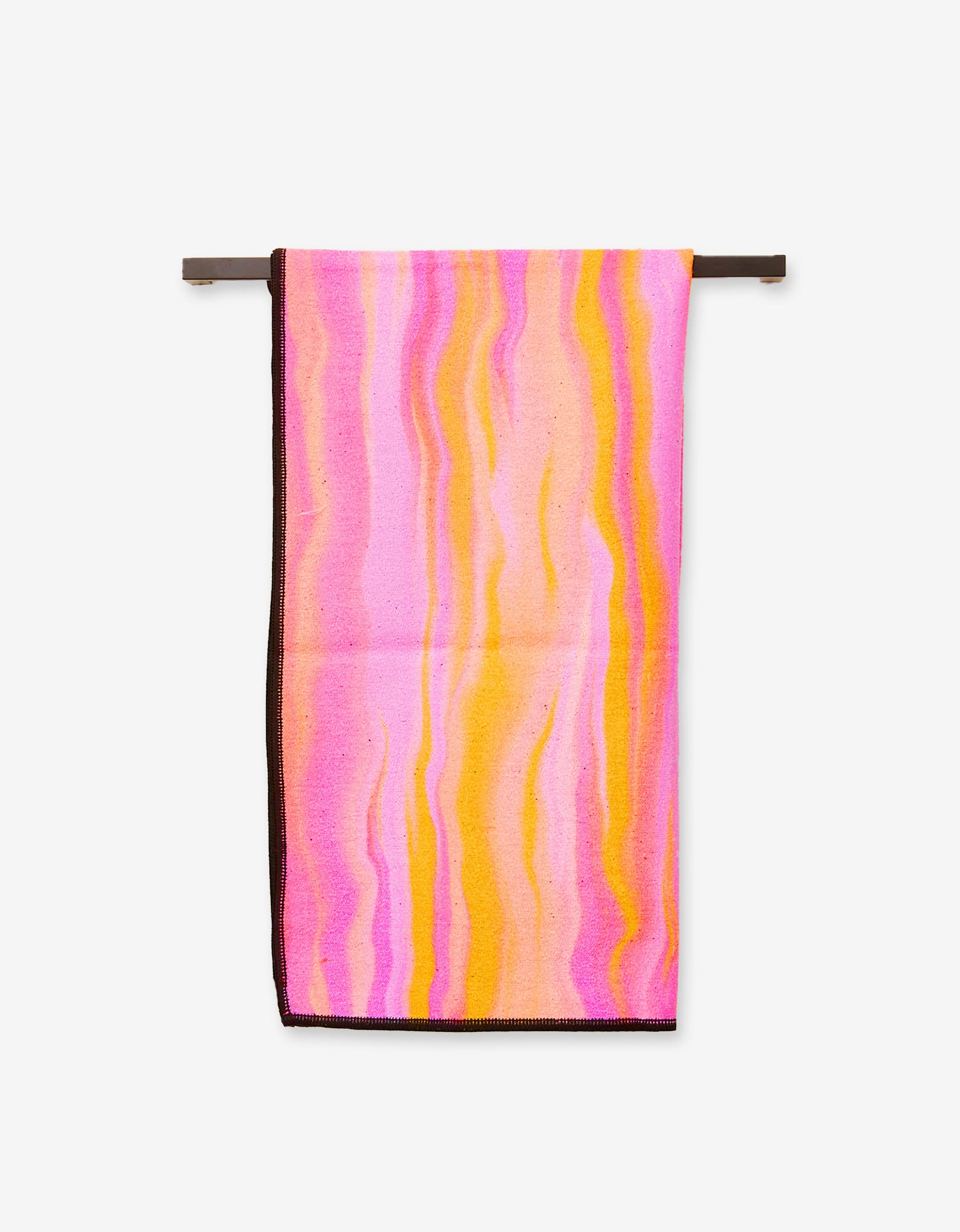 The Rush by GEOMETRY, an ultra-absorbent towel featuring a wavy, marbled pattern in pink, yellow, and orange tones, hangs neatly on a horizontal bar against a plain white background.