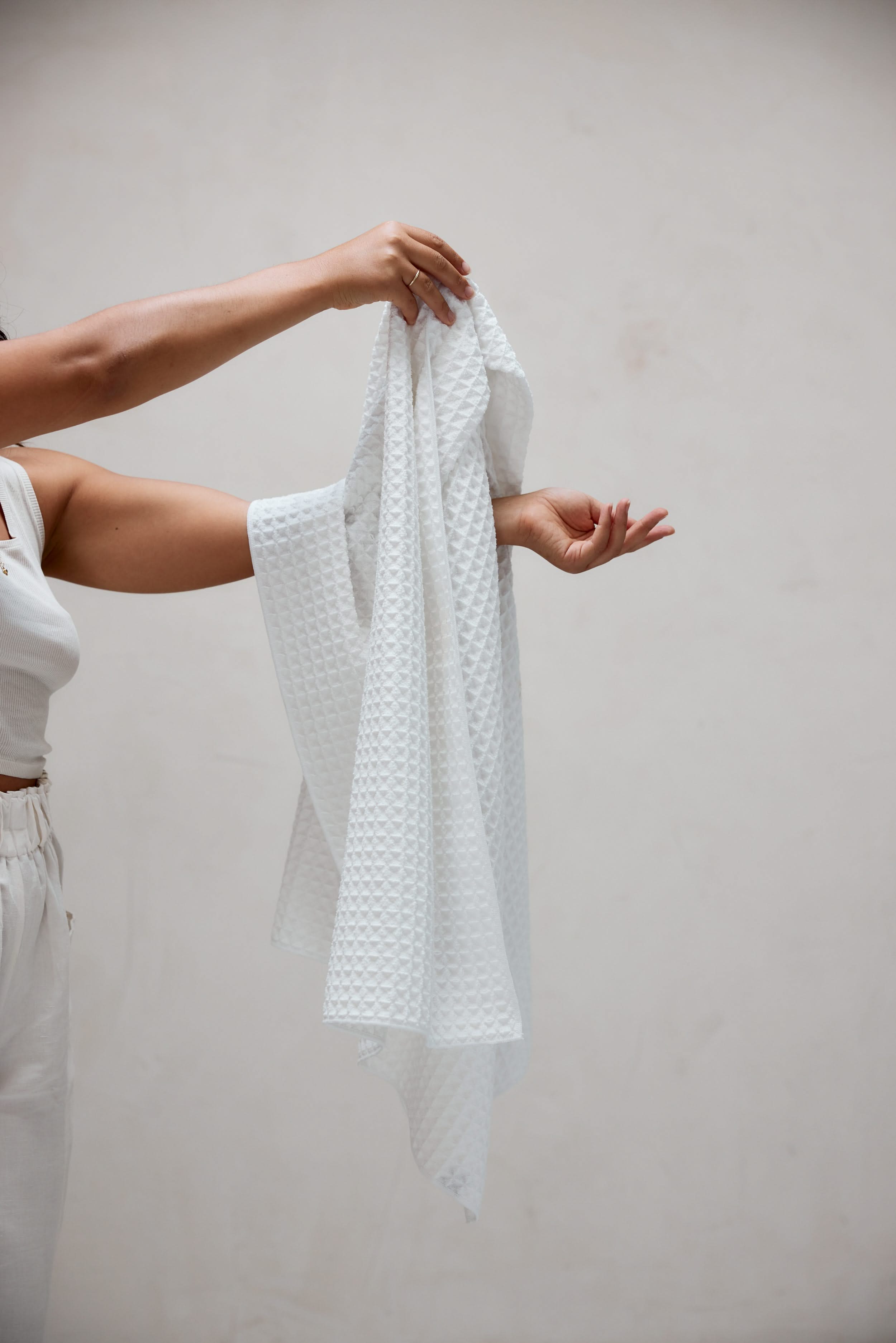 A person dressed in white holds up the GEOMETRY Cloud Waffle Bath Towel with both hands against a plain light background, showing only their upper body and arms.