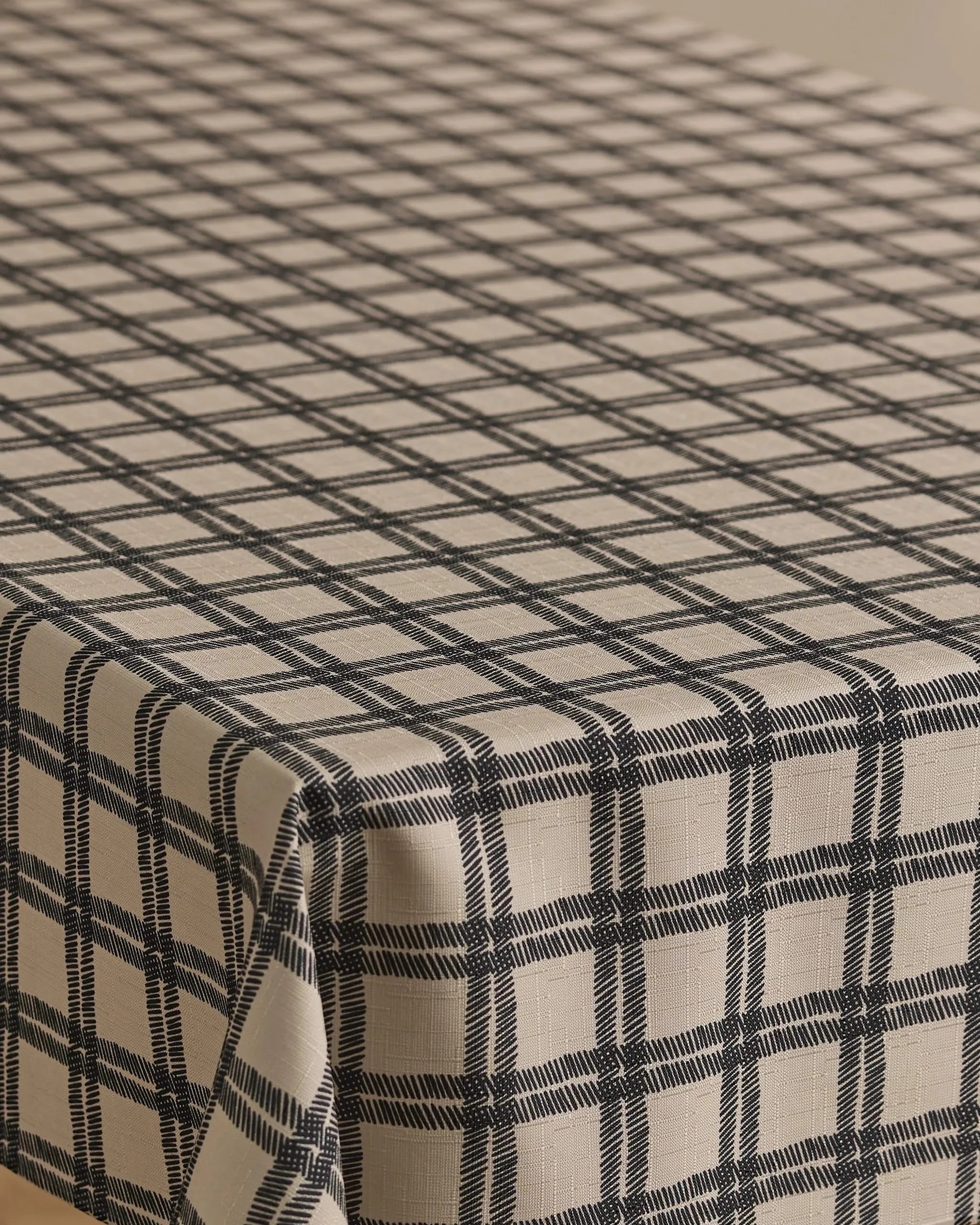 A rectangular table is draped with the Geometry Blackstone tablecloth, a beige, stain-resistant cover featuring an evenly spaced black checkered pattern.