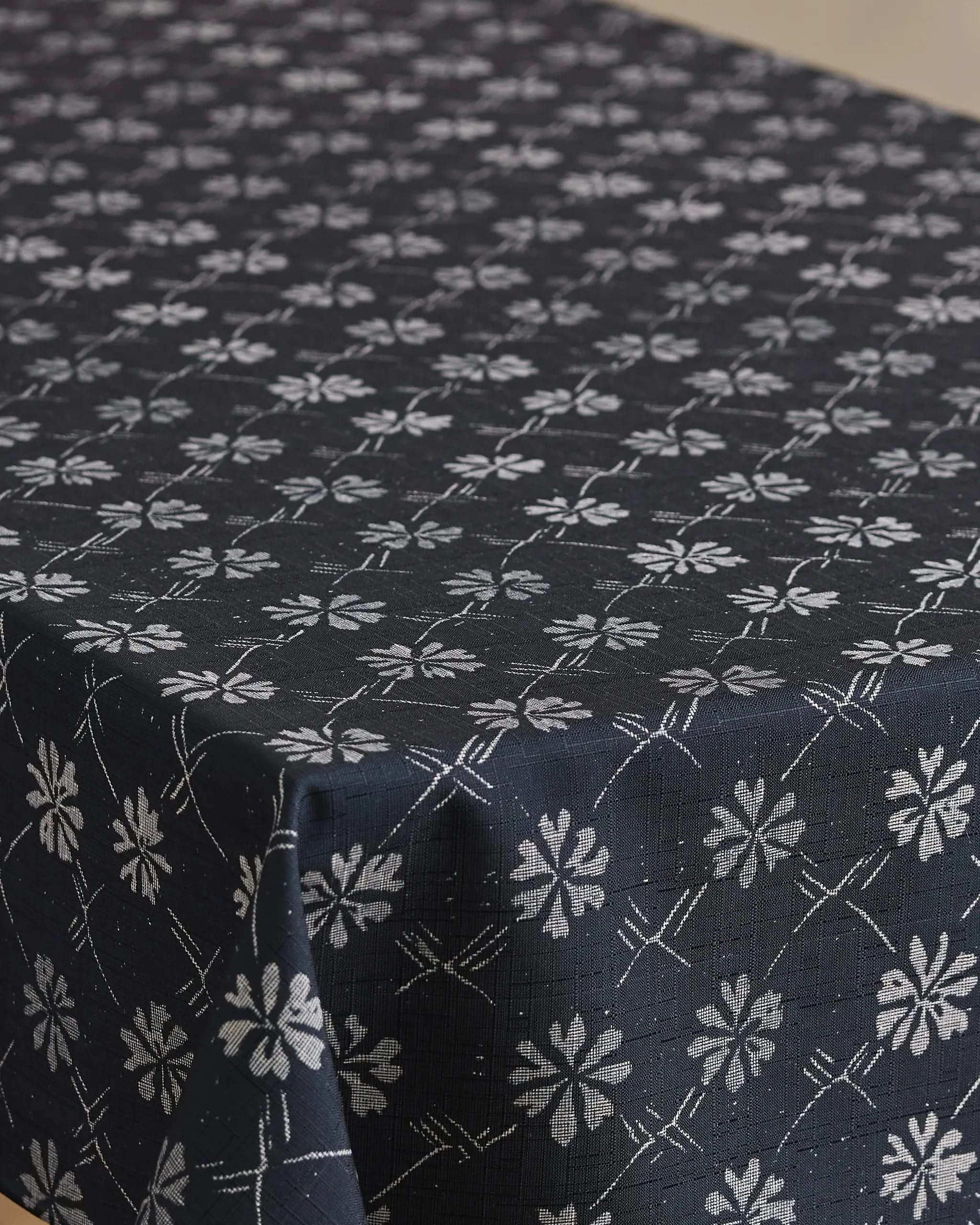 The Bonnie Indigo tablecloth by Geometry features a dark blue, stain-resistant design with a repeating white floral pattern and diagonal lines, neatly draped over a table.