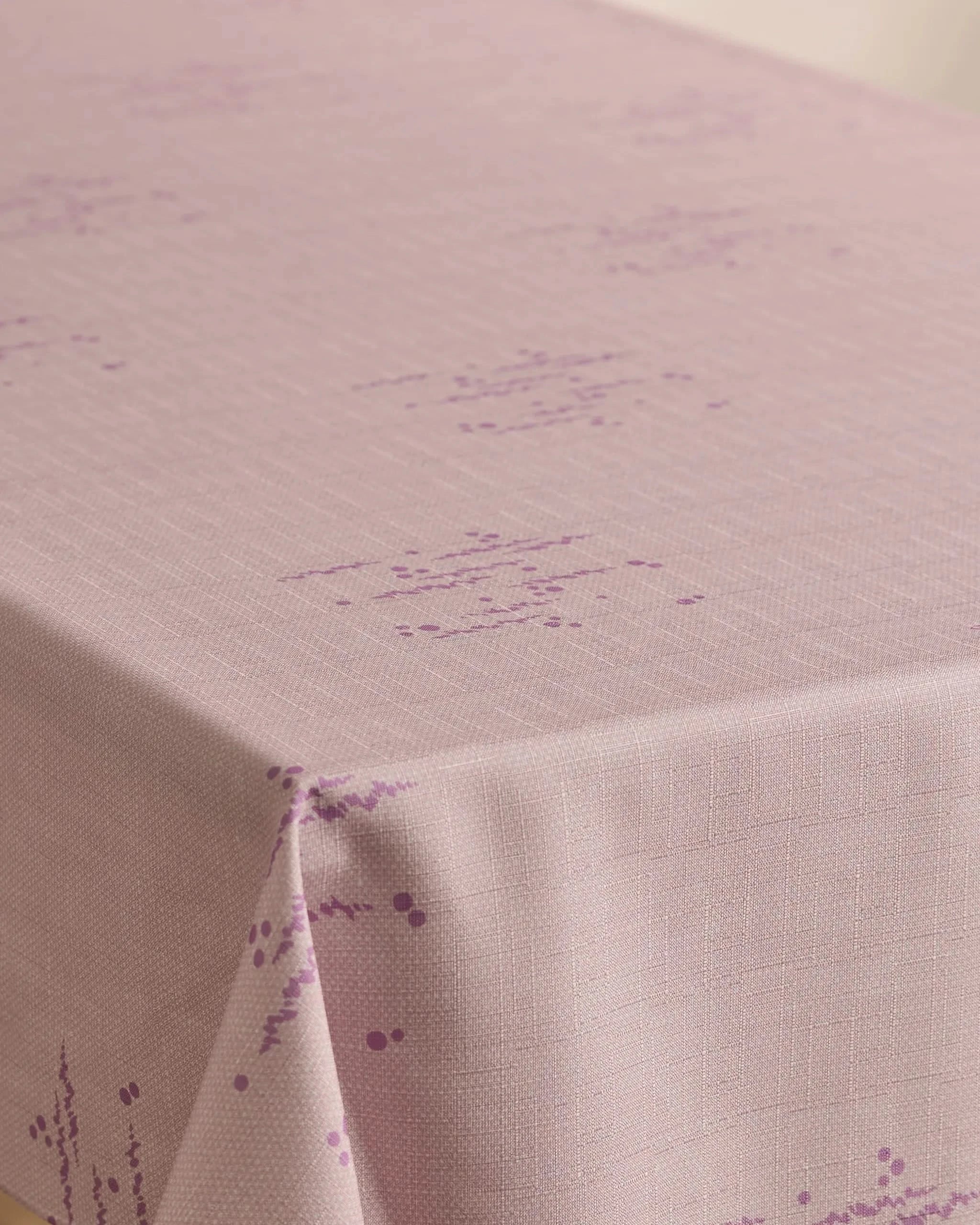 A Bubble Ditzy Dusty Rose tablecloth by Geometry, featuring stain resistance, a subtle grid texture, and small purple geometric patterns, is neatly draped over a table corner.