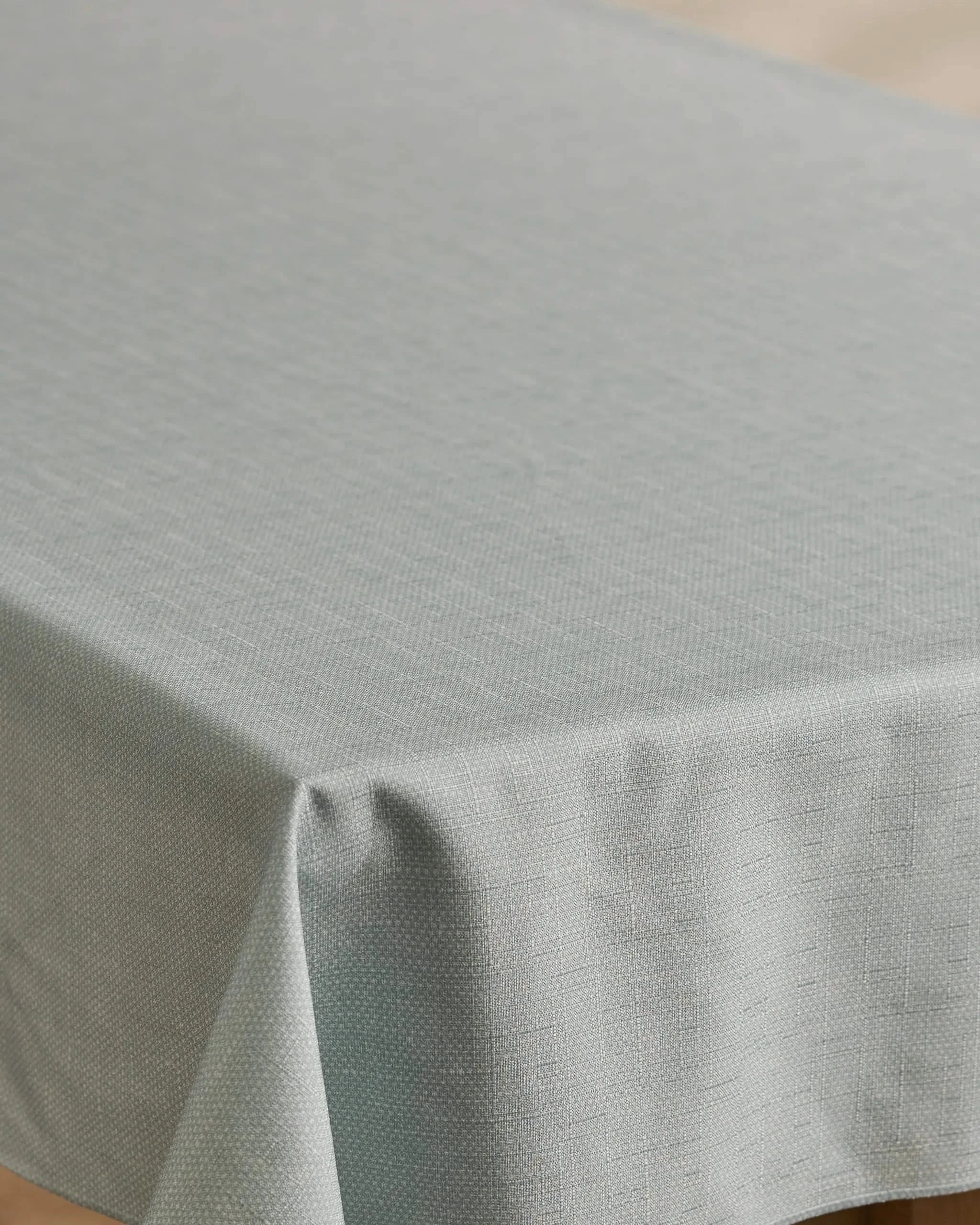 A close-up of Geometry’s Chambray Light Blue tablecloth, stain-resistant and neatly draped over a rectangular table, showcasing its soft folds along the edges.