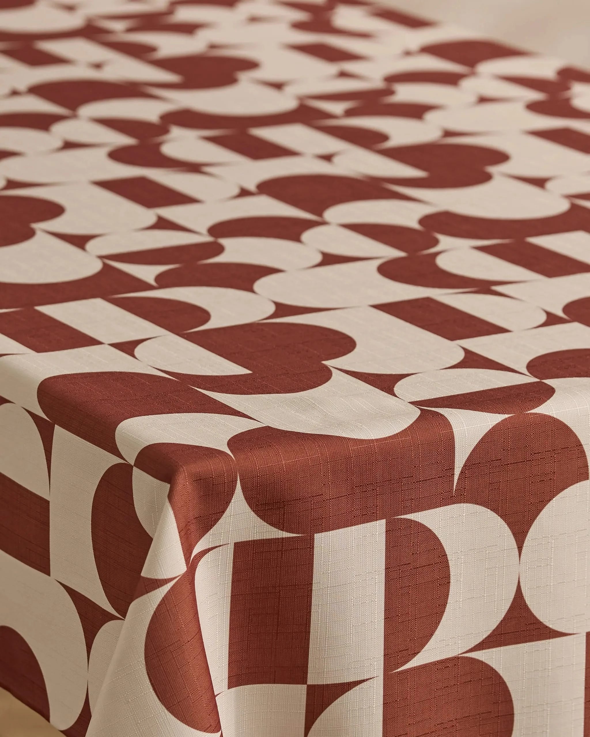 A table covered with Geometry’s Circle Playground cream-colored, stain-resistant tablecloth, featuring a bold geometric pattern of large, overlapping red shapes and arches.