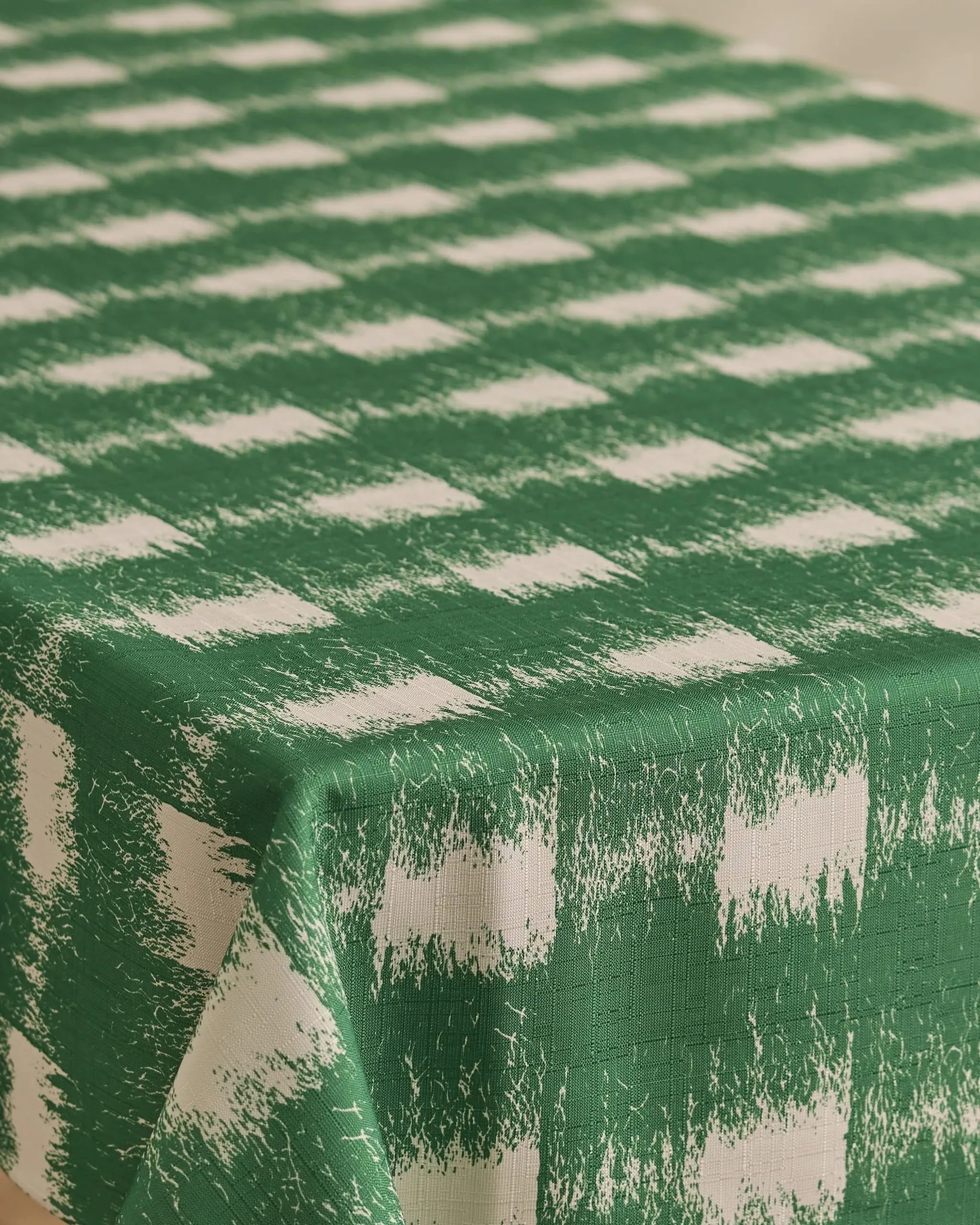 The Geometry Hairy Check Green tablecloth, featuring a green and white checkered distressed pattern, is stain-resistant and drapes elegantly over rectangular tables.