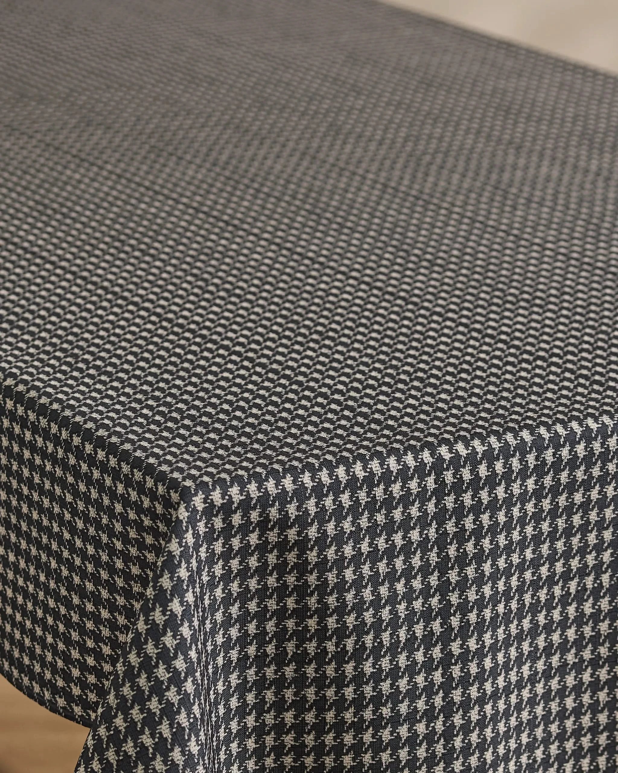A close-up of a table covered with Geometry’s Houndstooth Black tablecloth, featuring its lightweight fabric and crisp black and white houndstooth pattern draping smoothly over the softly rounded edge.
