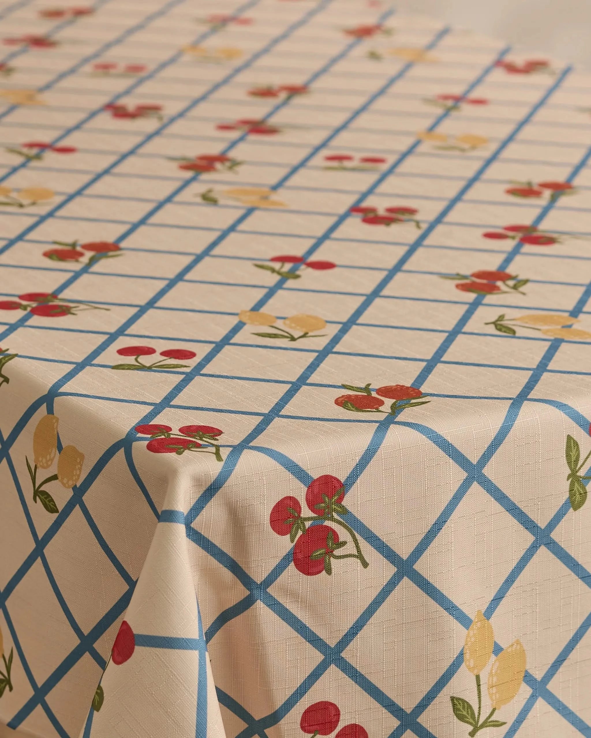 The Geometry Italian Summer Grid tablecloth, in beige with a blue grid and red cherries with yellow lemons print, offers a lightweight, stain-resistant cover for your rectangular table.
