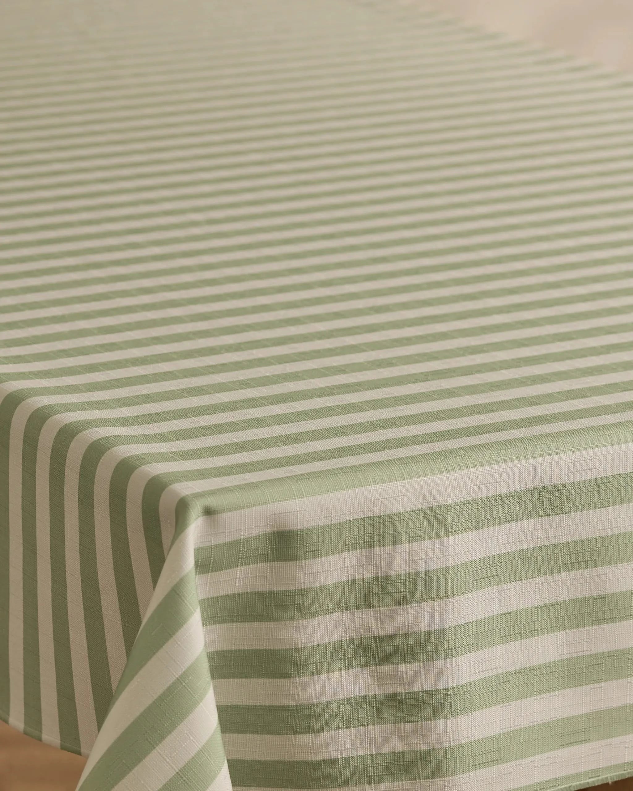 A close-up of a rectangular table covered with the Geometry Seagrass tablecloth, featuring green and white horizontal stripes on top and vertical stripes along the edge. This stain-resistant tablecloth combines style with practicality.