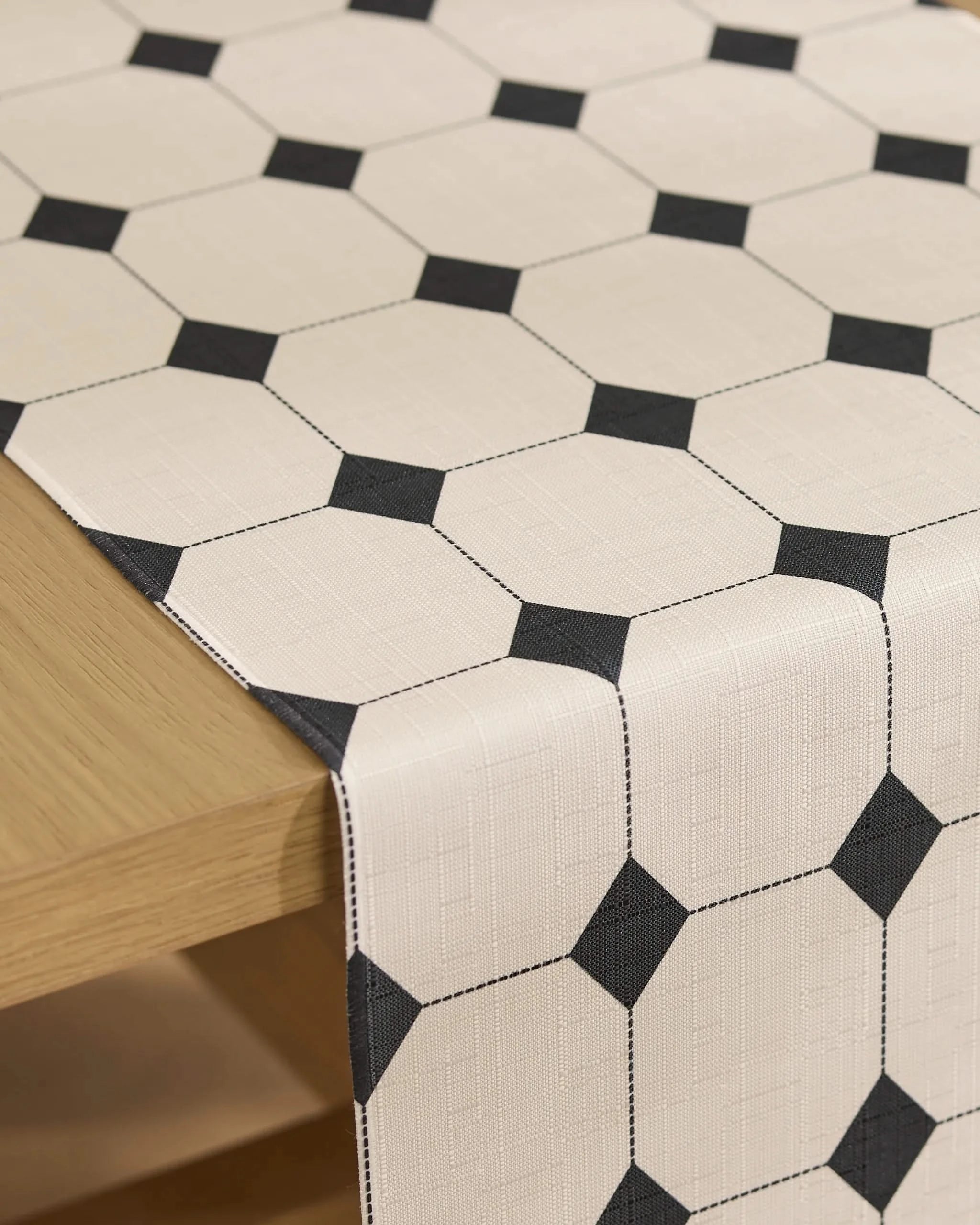 A Geometry Espresso Mosaic table runner with an octagon and small black square pattern is draped over a light wooden table.