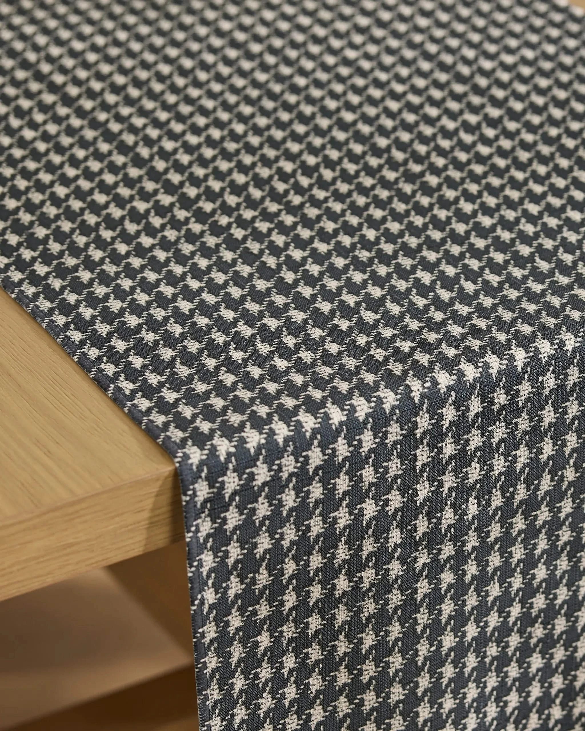 A close-up of Geometry’s Houndstooth Black stain-resistant table runner, showcasing its black and white pattern draped over a light wood table.