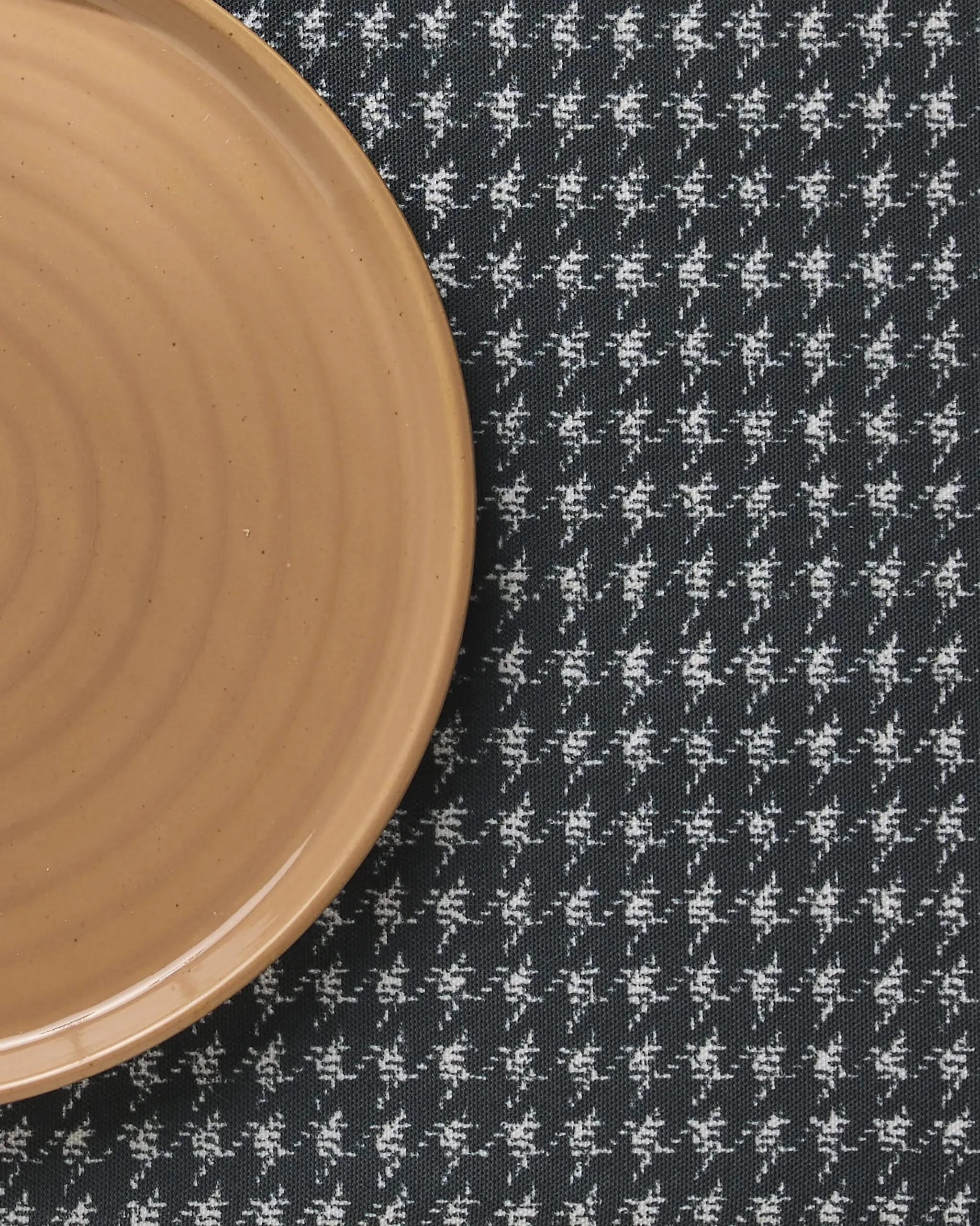 A partial view of Geometrys Houndstooth Black round ceramic plate on a matching black and white houndstooth tablecloth—perfect for effortless style, especially when paired with Geometry Placemats or other recycled placemats.