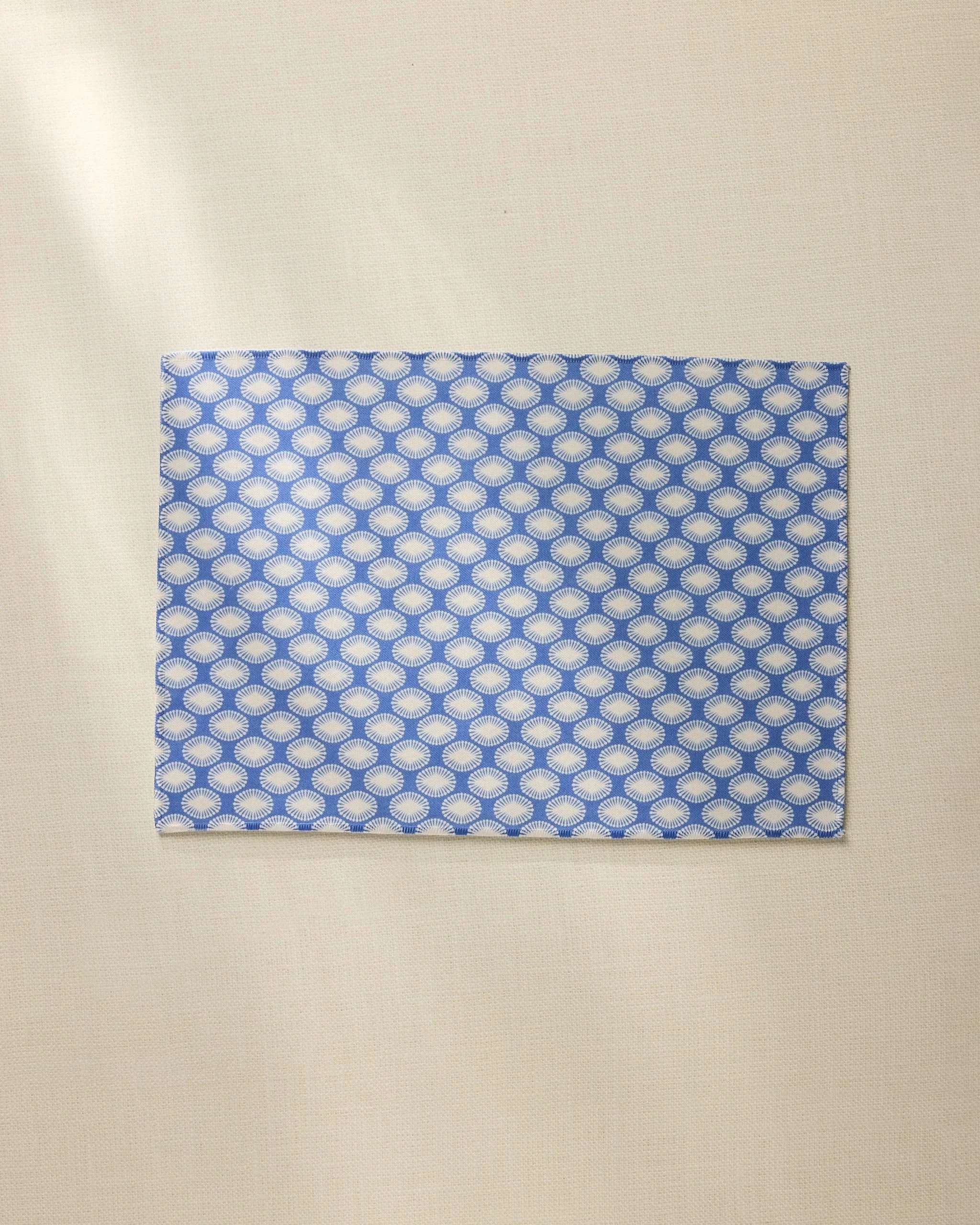 The Geometry Lagoon is a rectangular, machine washable placemat featuring a blue and white geometric design, shown lying flat on a light beige surface.