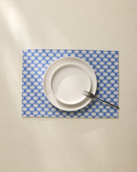 A white plate and small bowl stacked with a fork on the edge sit on a cream tablecloth over stylish Geometry Lagoon Placemats in blue and white patterns.
