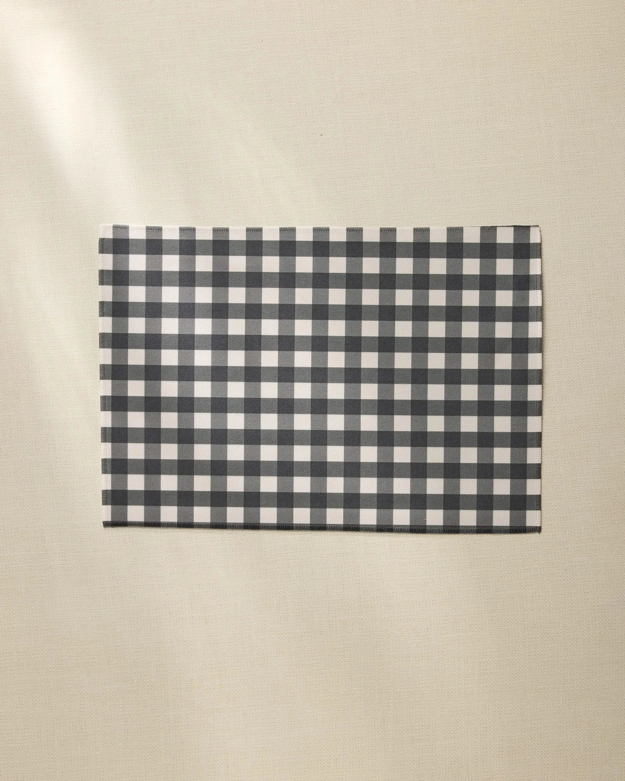 A Geometry Charcoal Gingham rectangular placemat is placed on a light beige textured surface.