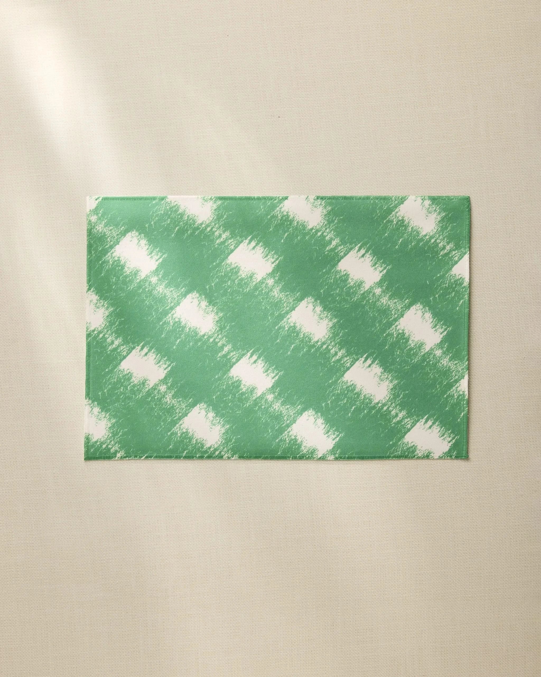 The Hairy Check Green placemat by Geometry features a white brushed checkered pattern on green, shown on a beige surface. Made from recycled materials, this everyday placemat is easy to clean and perfect for daily use.
