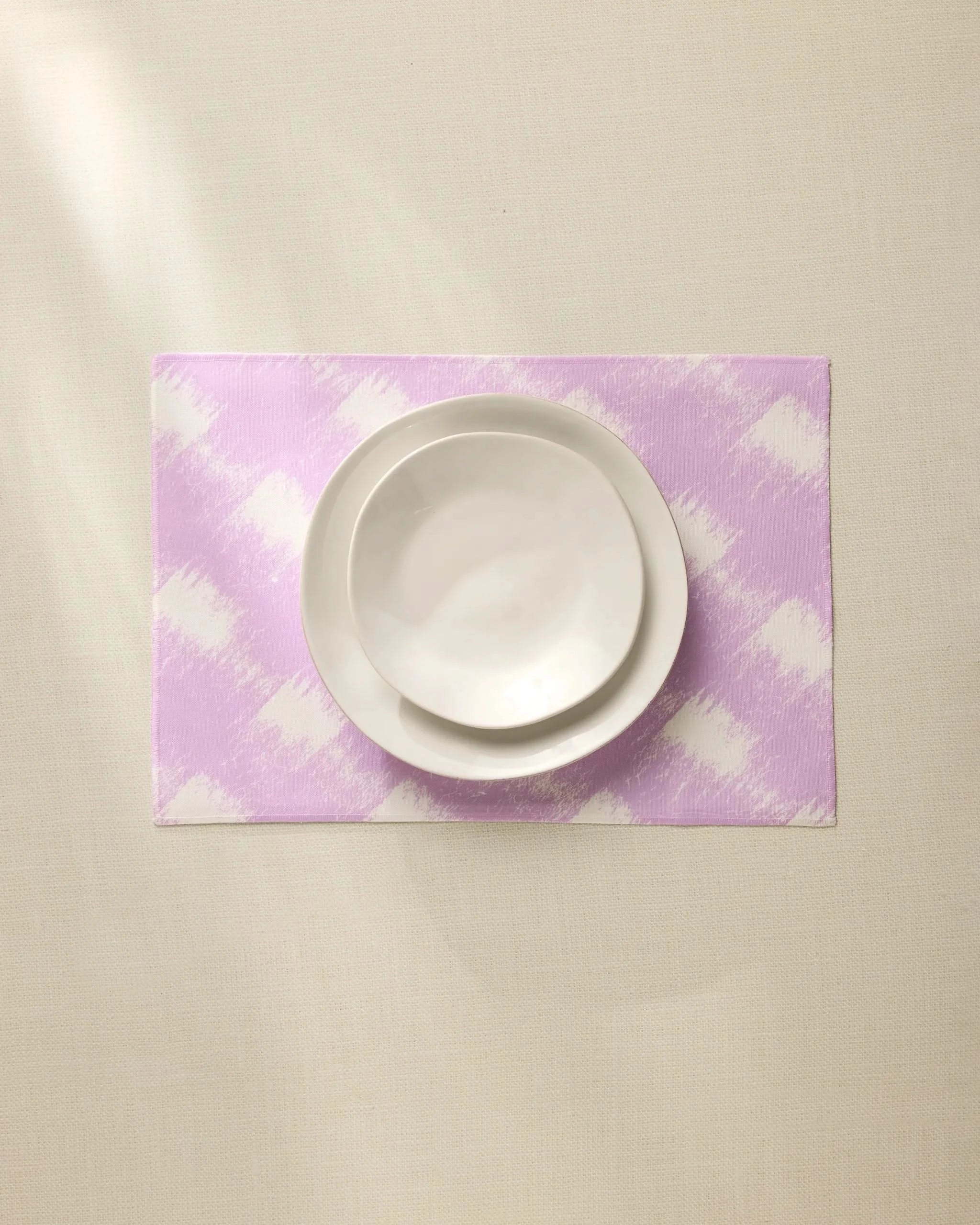 A white bowl and plate are stacked on the Geometry Hairy Check Pink recycled placemat, set on a light beige surface under soft lighting.