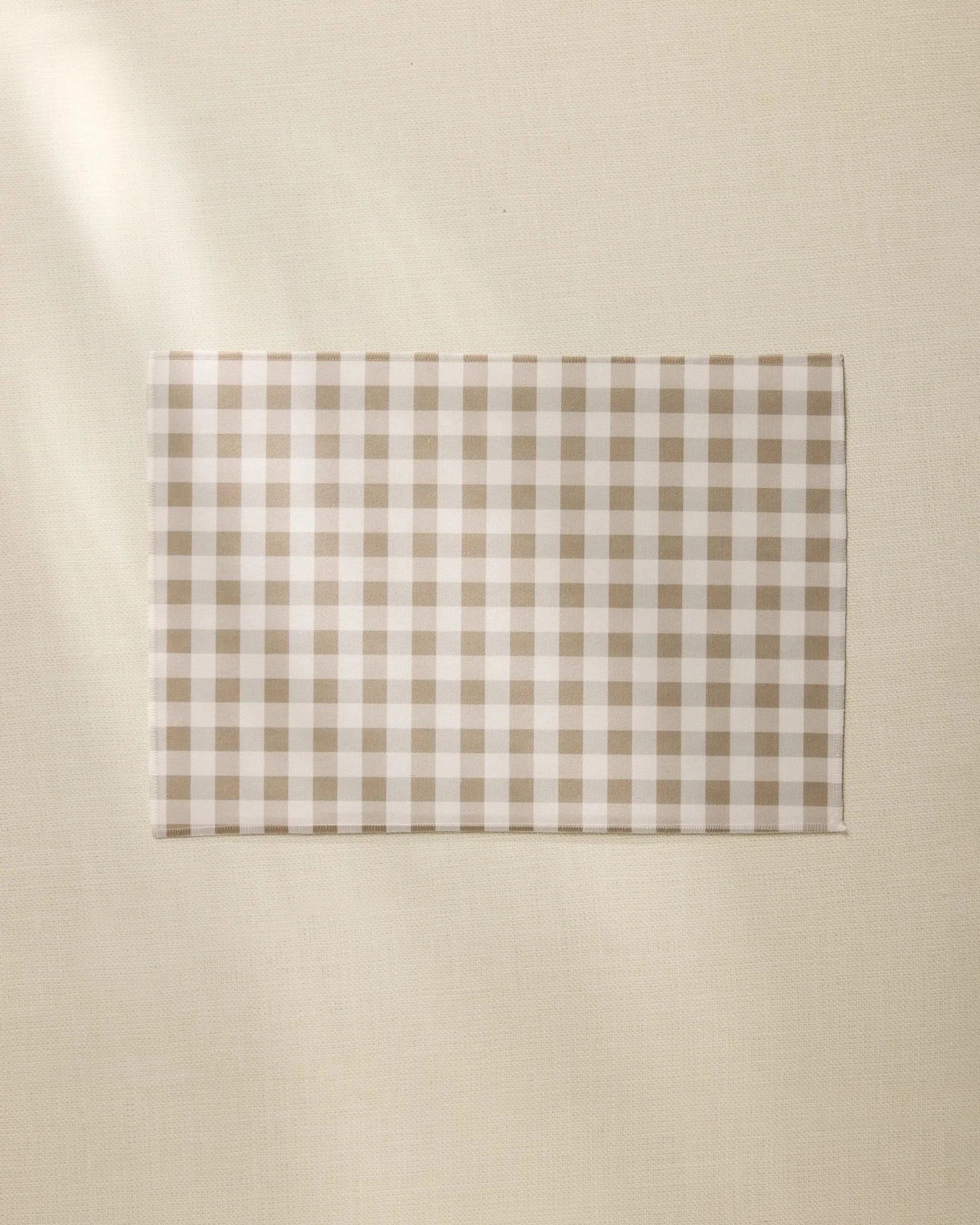 The Hazel Gingham napkin by Geometry, featuring a beige and white checkered design like our recycled placemats, is neatly displayed on a light, textured surface.
