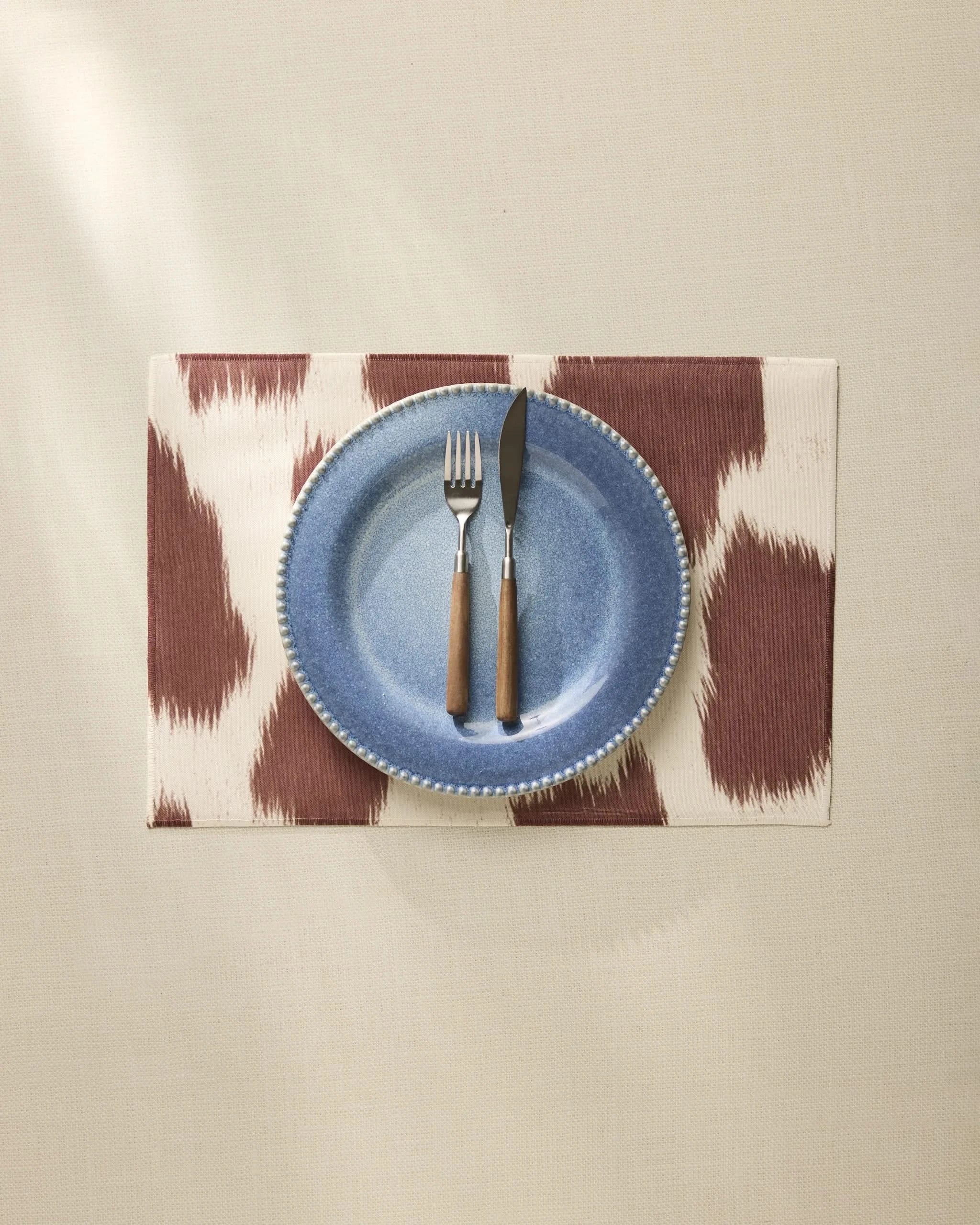 A blue ceramic plate with a fork and knife sits on Geometry’s Rodeo machine-washable placemat atop a beige tablecloth.