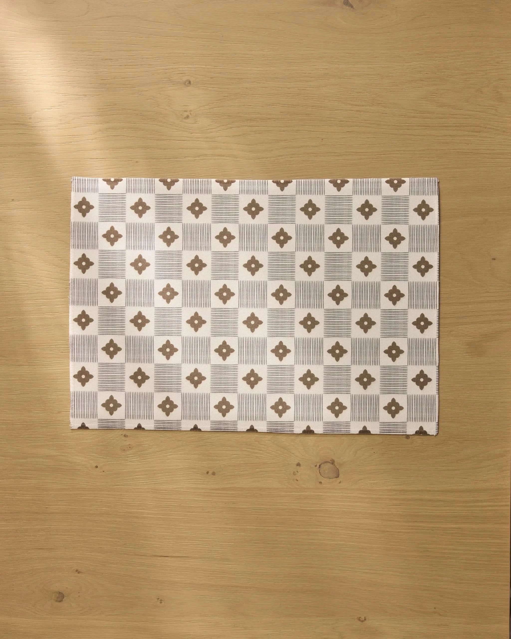 The Legacy Block by Geometry is a rectangular, geometric brown and white patterned recycled placemat, stylishly displayed on a light wooden surface for eco-friendly table decor.