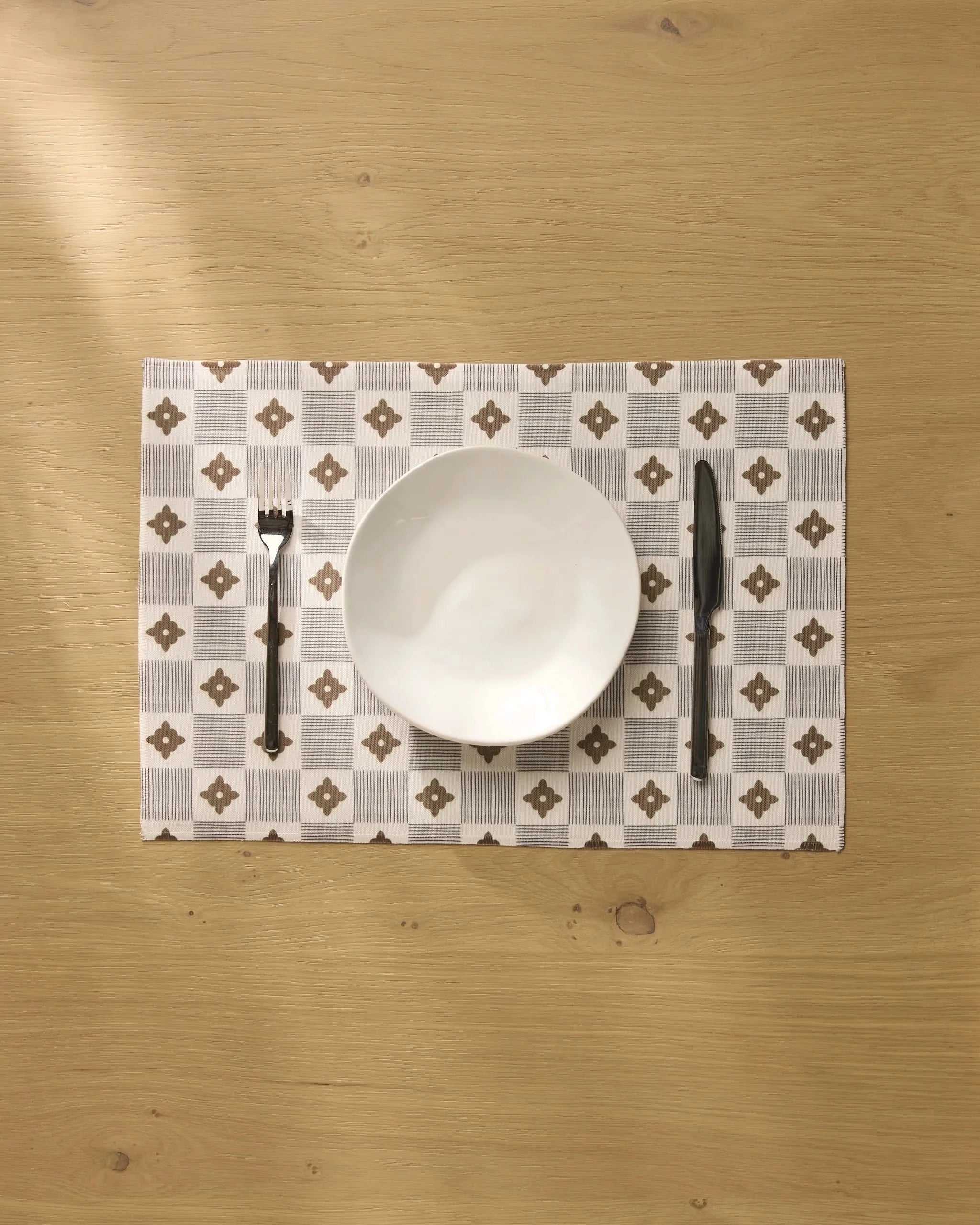 A white bowl is placed on the Geometry Legacy Block placemat, with a fork to the left and a knife to the right, all neatly arranged on a light wooden table.