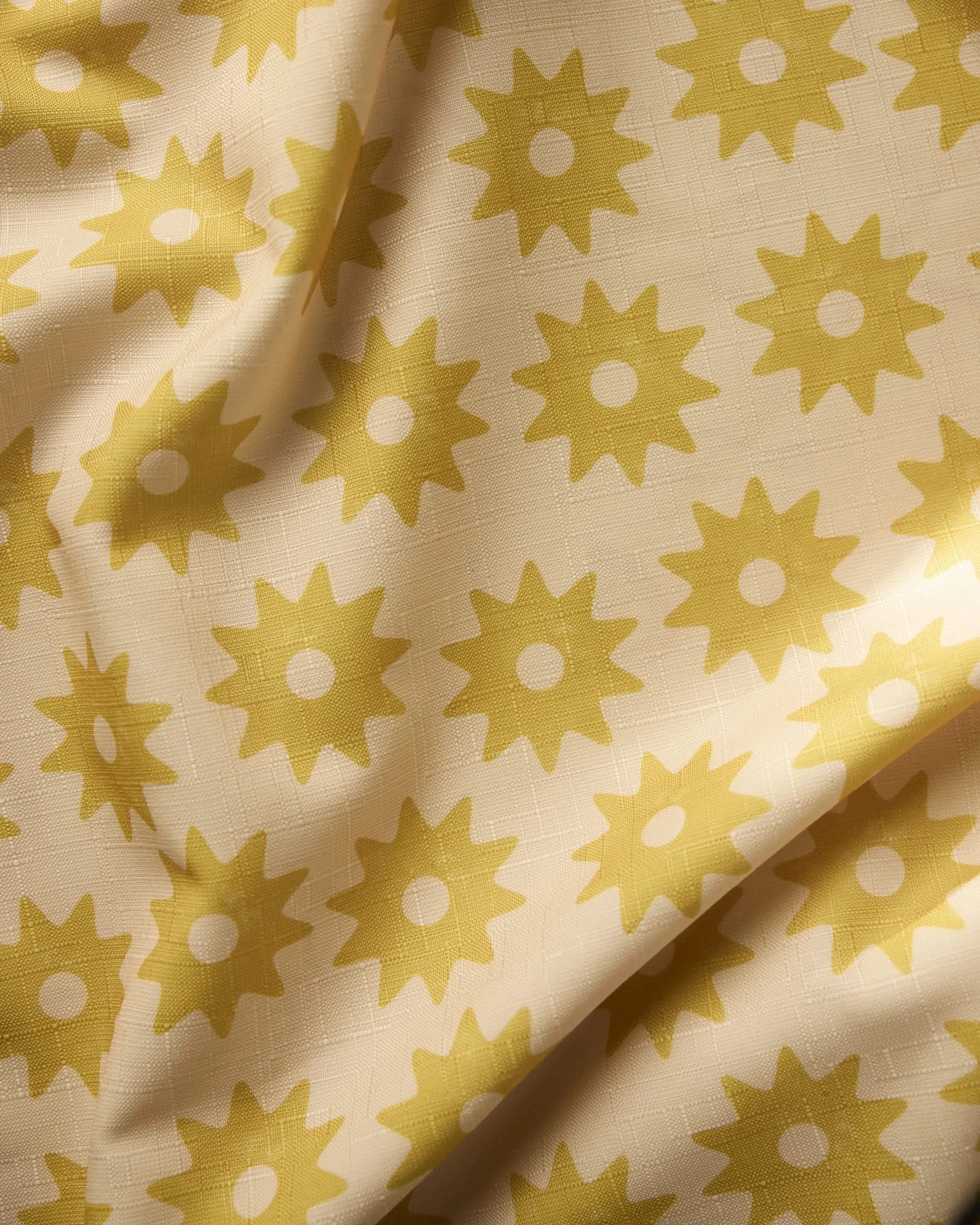 A close-up of Geometrys Sunny Sun tablecloth fabric in cream, featuring a lightweight design with yellow sunburst patterns, gentle folds, and a subtle textured weave.