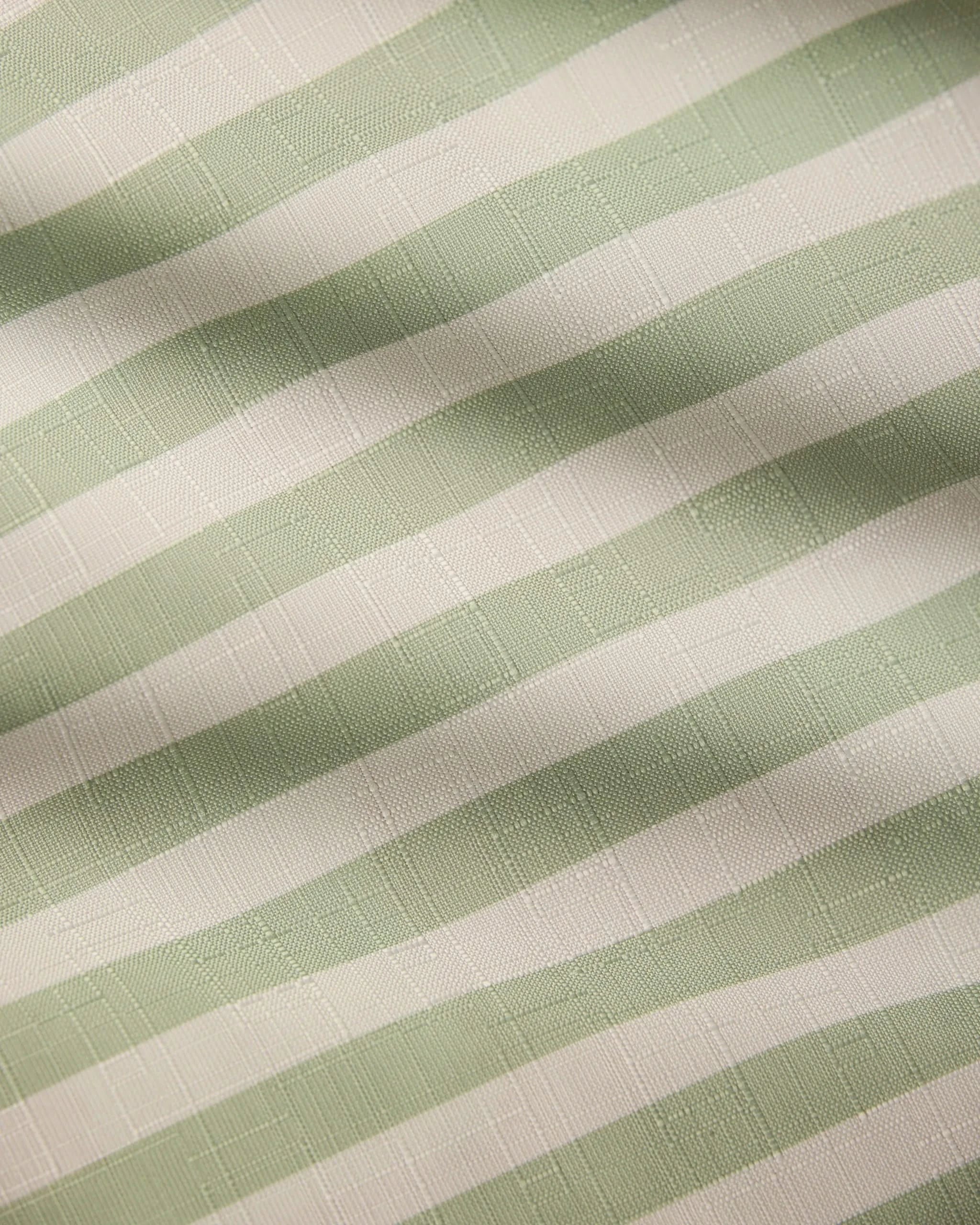 Close-up of Seagrass fabric by Geometry, featuring pale green and white horizontal stripes. Its subtle grid pattern and gentle folds make it ideal for a stain-resistant, recycled-material table runner.