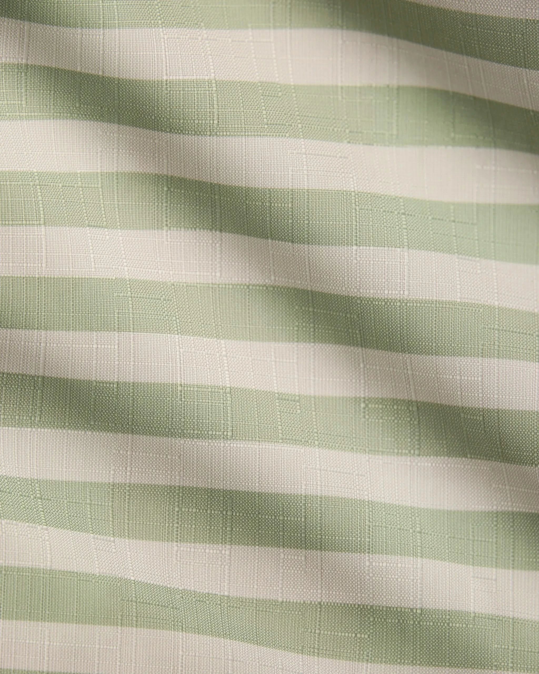 Seagrass by Geometry features light green and white horizontal stripes on textured, recycled tablecloth fabric, with soft waves and shadows adding gentle movement and depth.