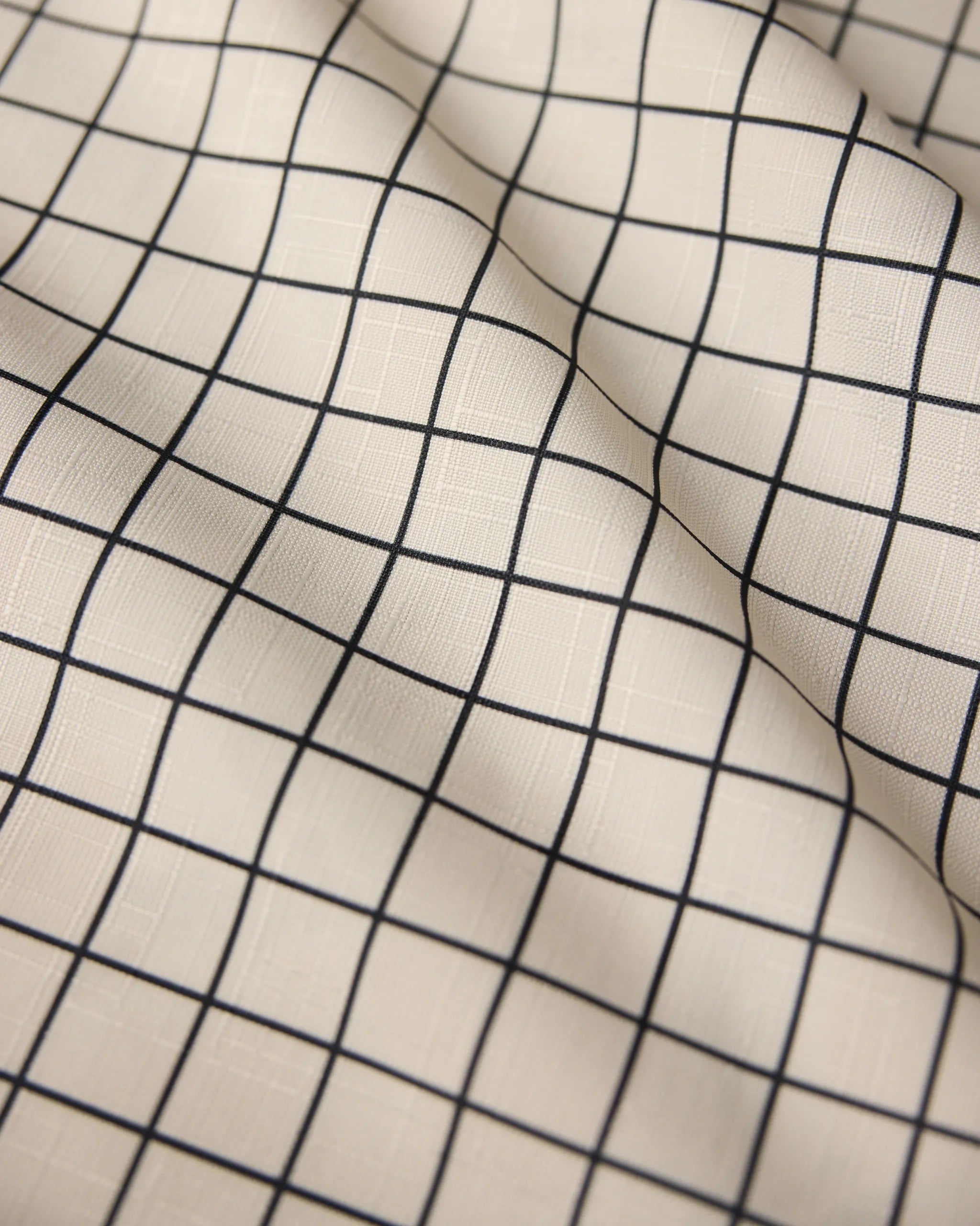 The Geometry Metro Grid table runner features cream-colored, stain-resistant fabric with a black grid of evenly spaced squares, creating gentle folds and subtle shadows for a stylish, modern look.