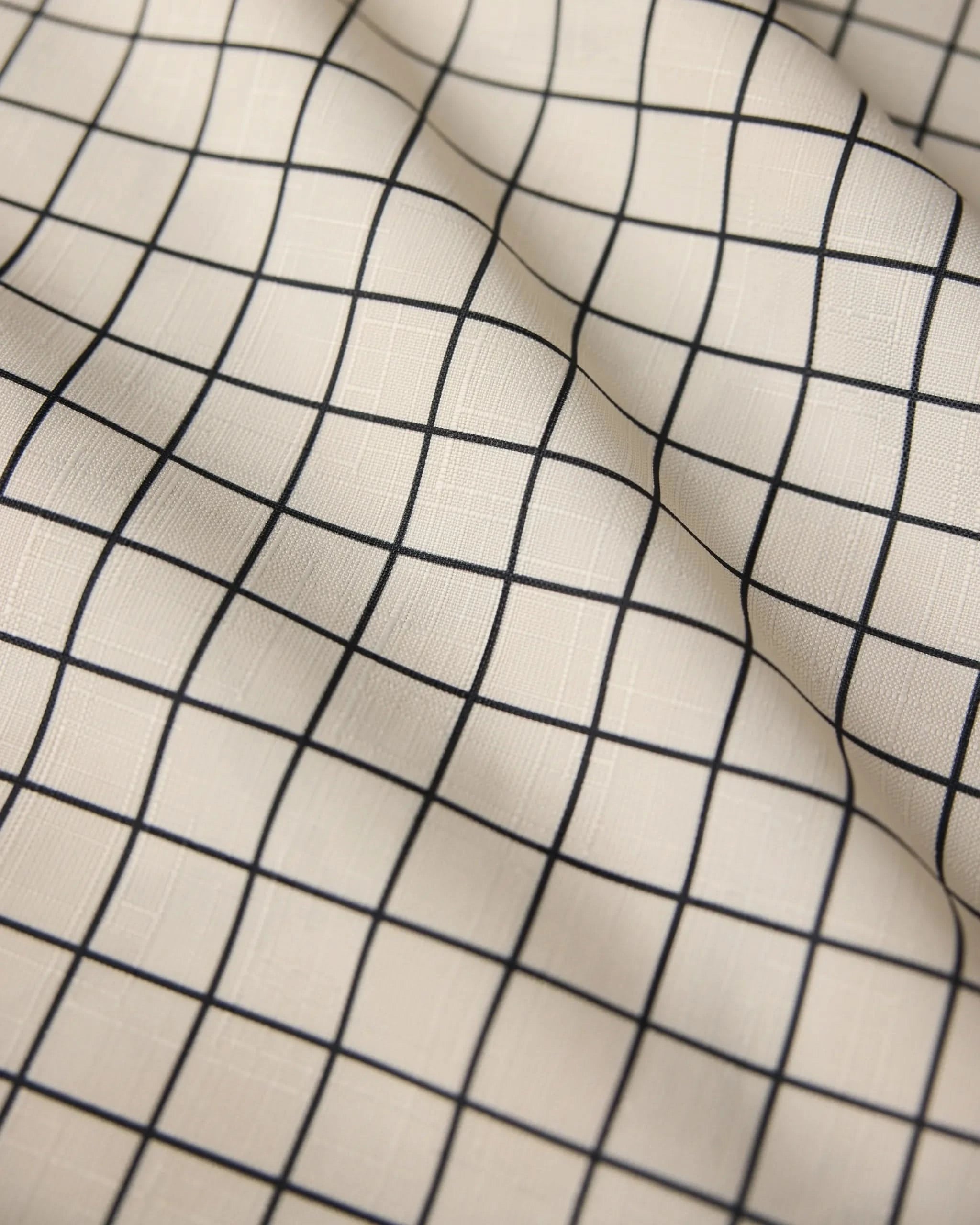 The Geometry Metro Grid table runner features cream-colored, stain-resistant fabric with a black grid of evenly spaced squares, creating gentle folds and subtle shadows for a stylish, modern look.