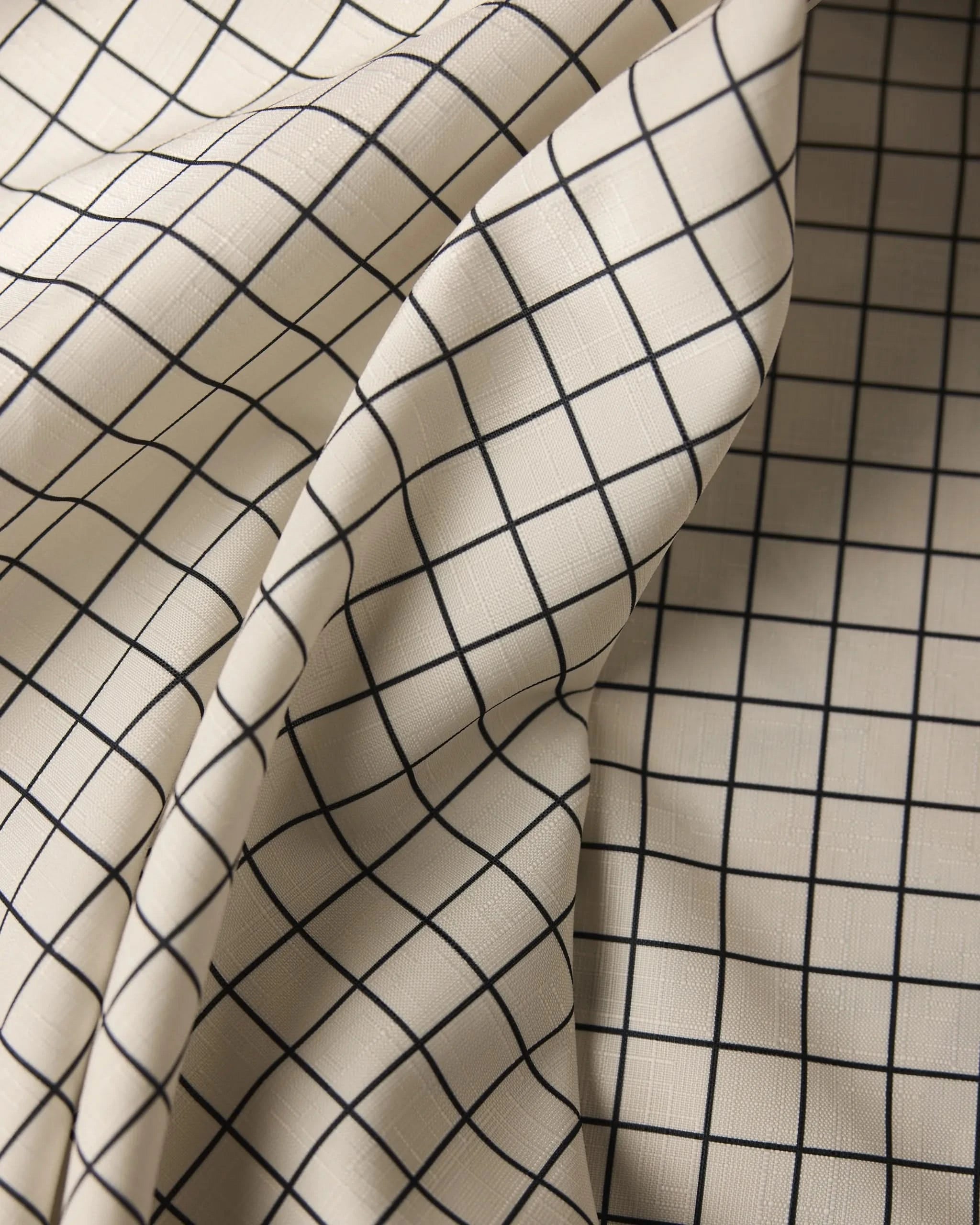 Geometry’s Metro Grid tablecloth is cream-colored, stain-resistant, and features a black grid pattern with evenly spaced lines and gentle folds that add shadow and texture.