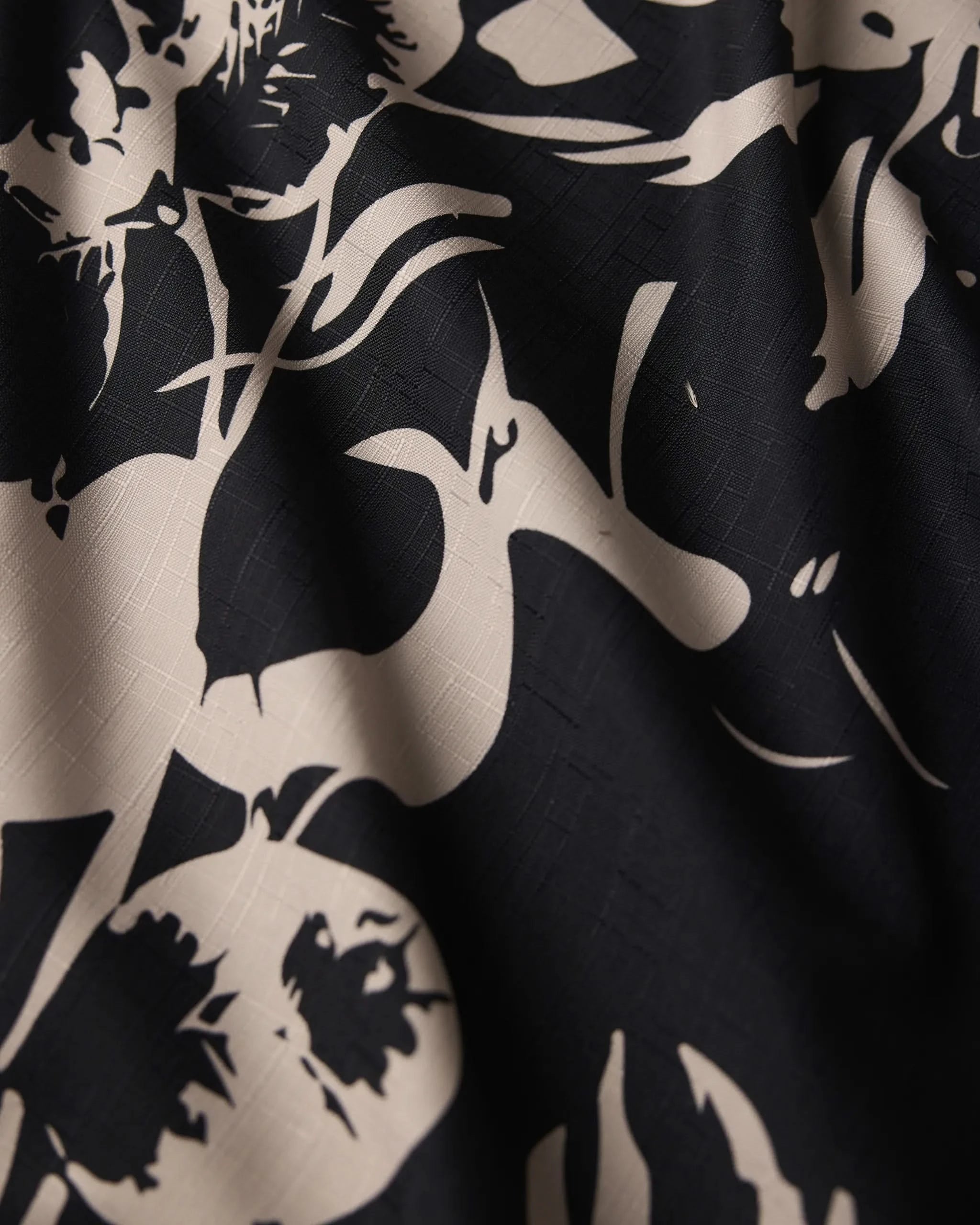 Close-up of Geometry’s Inverted Floral Black tablecloth: black recycled fabric with a beige floral pattern, featuring abstract leaves and flowers. Soft, wavy texture and a subtle grid-like weave appear in the lighter sections.