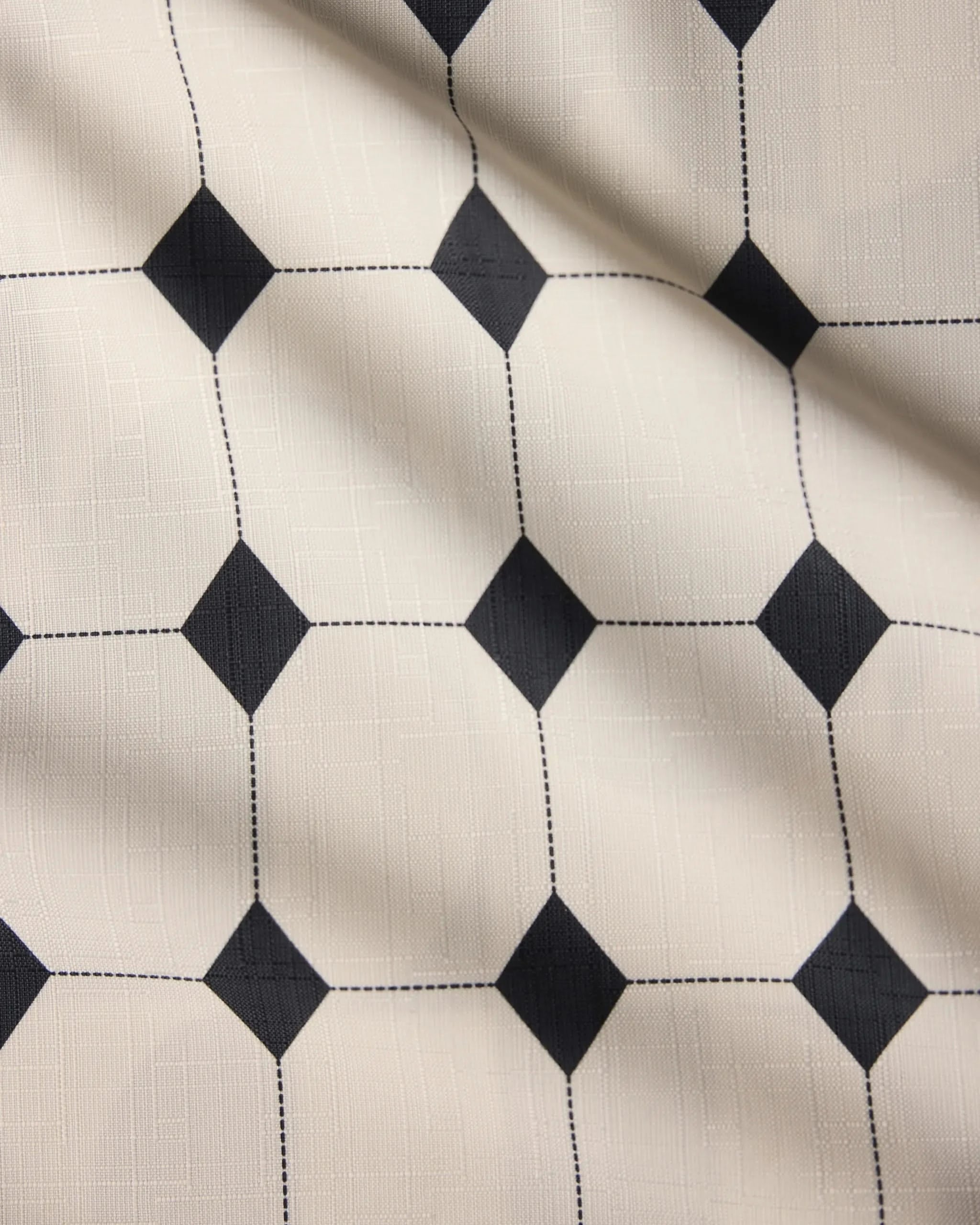A close-up of the Espresso Mosaic table runner by Geometry, featuring a cream base with black diamond patterns and thin dotted grid lines, highlighting its gentle folds and textured fabric.