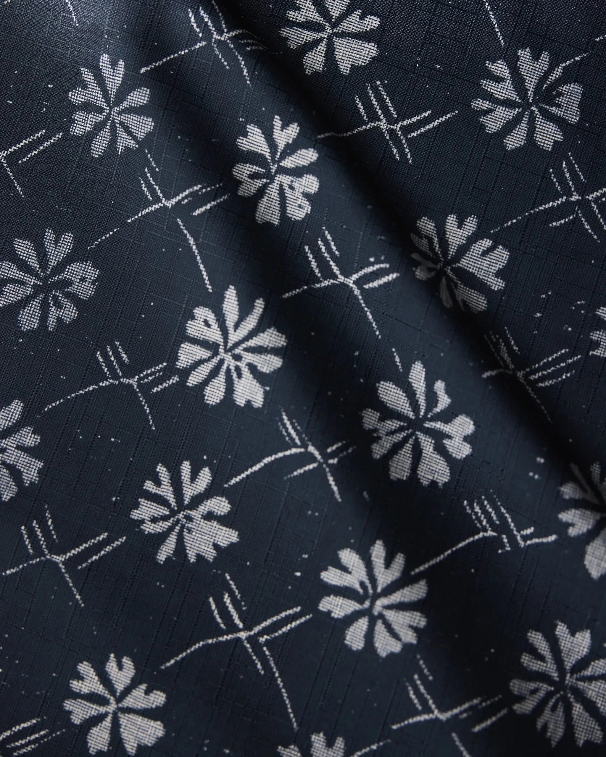 A close-up of Bonnie Indigo by Geometry—dark blue fabric with a white geometric floral pattern and intersecting lines, highlighting its stylish texture and gentle folds for a practical, elegant table runner.