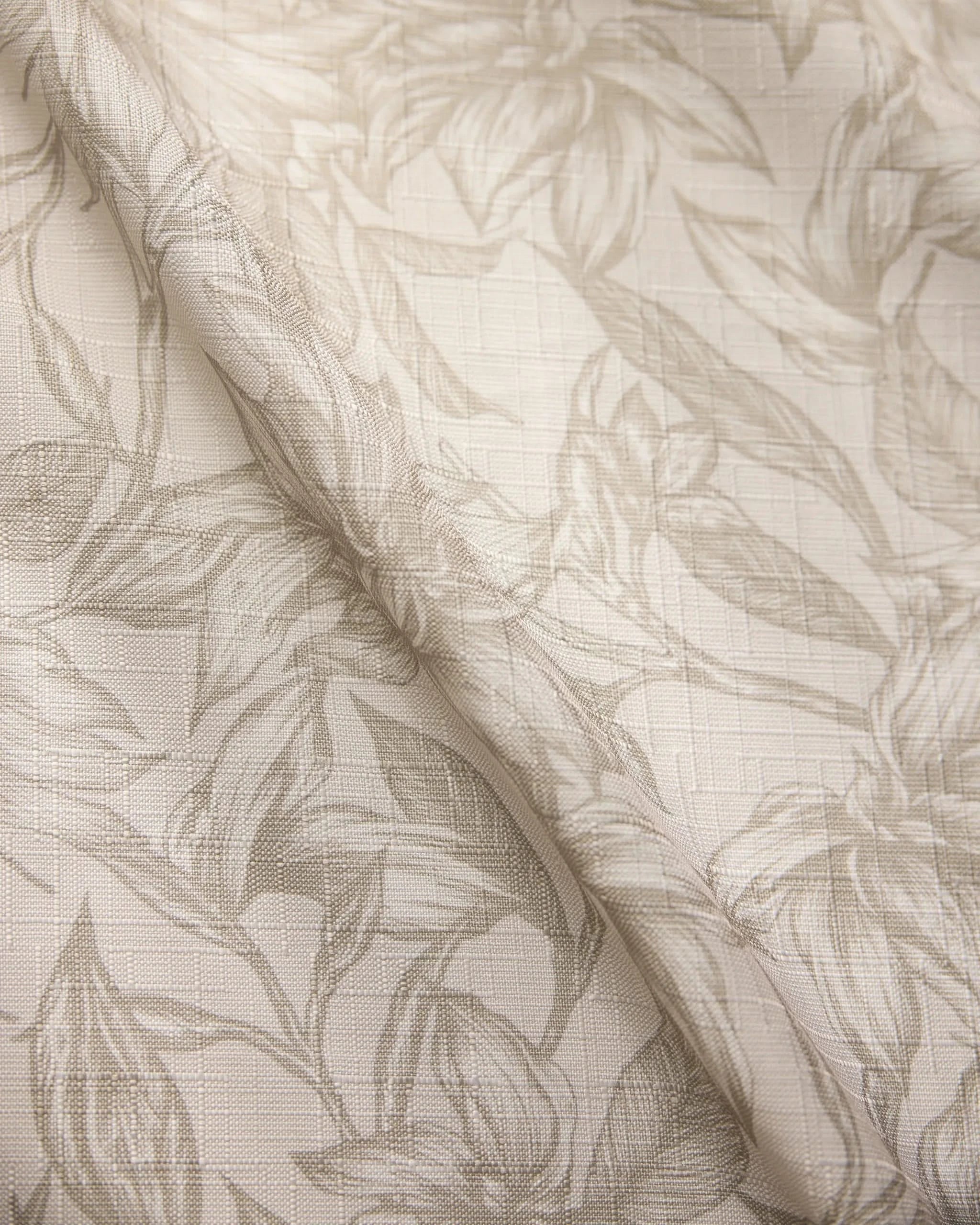 The Geometry Alba table runner features a light, stain-resistant fabric with a subtle floral leaf pattern and textured grid-like background for an elegant drape.