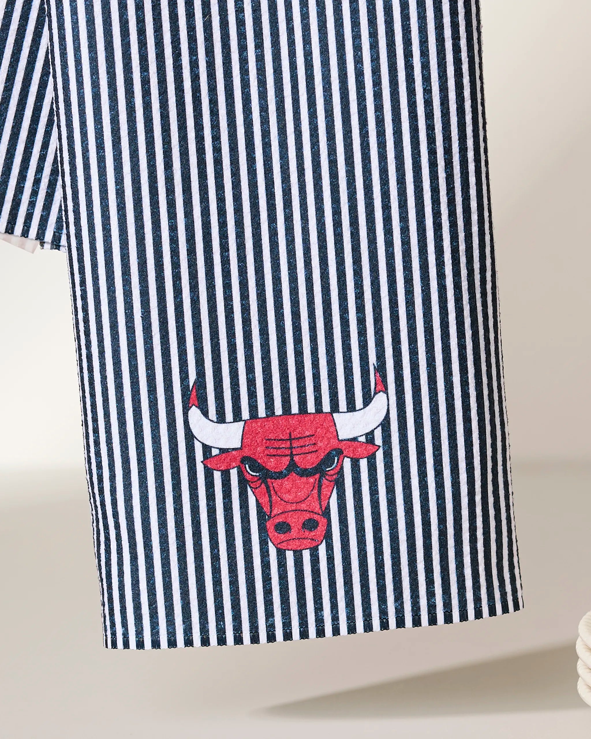 The Geometry Bulls Classic is a black and white vertical striped tea towel made from recycled materials, featuring the red and white Chicago Bulls logo embroidered near the bottom.