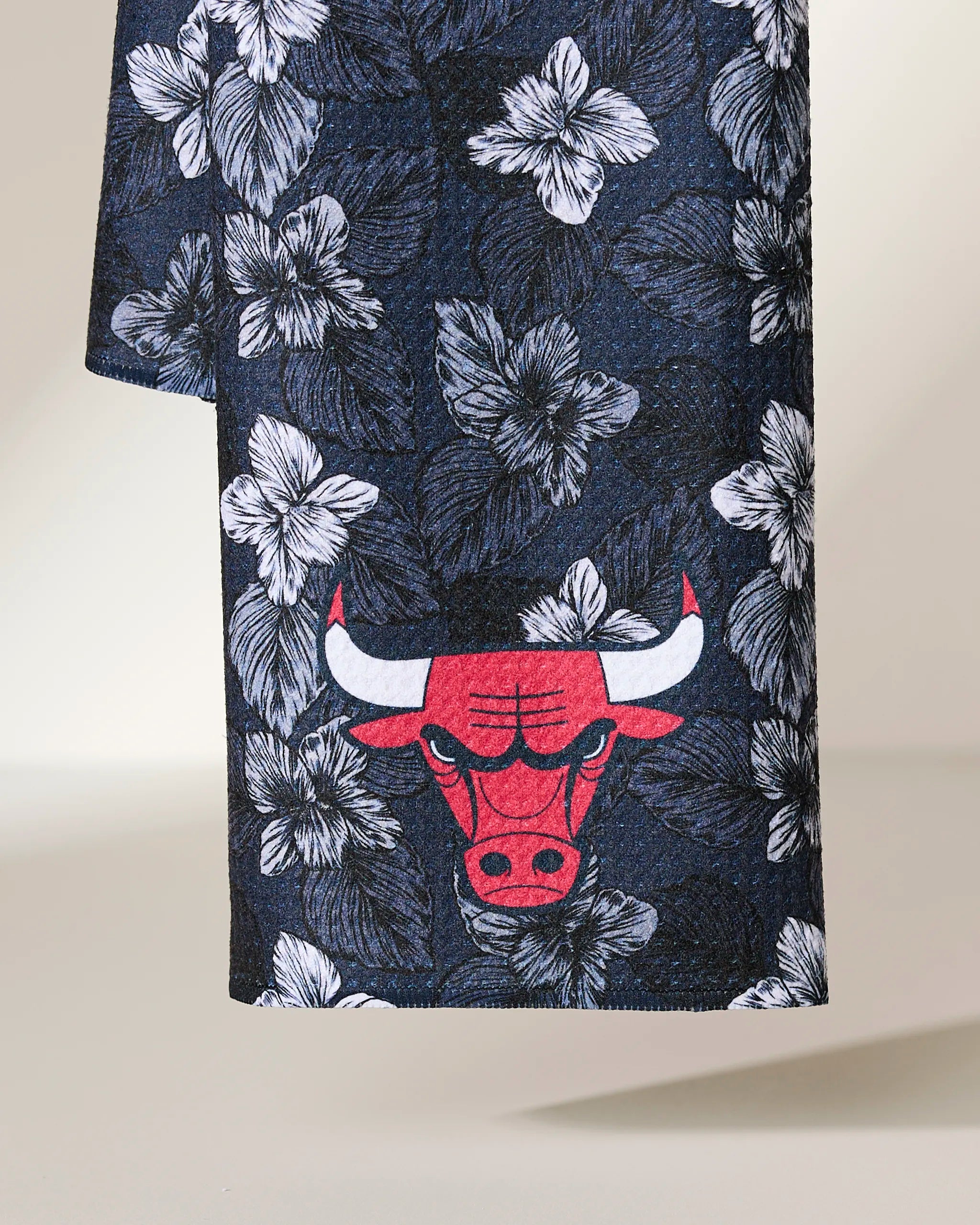 The Geometry Bulls Floral kitchen towel showcases a white hibiscus flower pattern on navy blue, accented by a red Chicago Bulls logo near the hem—perfect for adding team spirit to your kitchen.