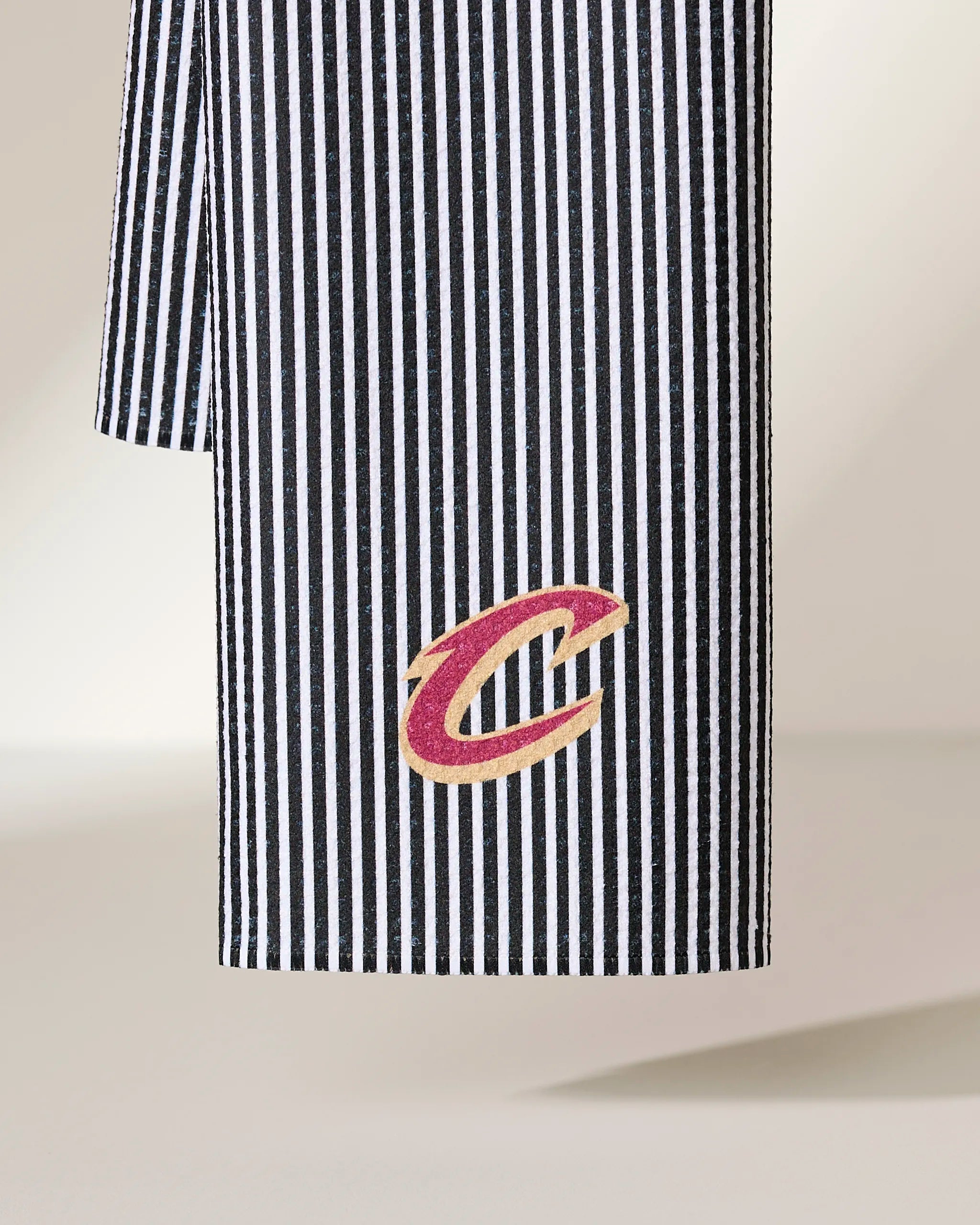 The Geometry Cavaliers Classic tea towel features black-and-white vertical stripes, is ultra-absorbent, made from recycled materials, and showcases the Cleveland Cavaliers red and gold C logo embroidered near the bottom.