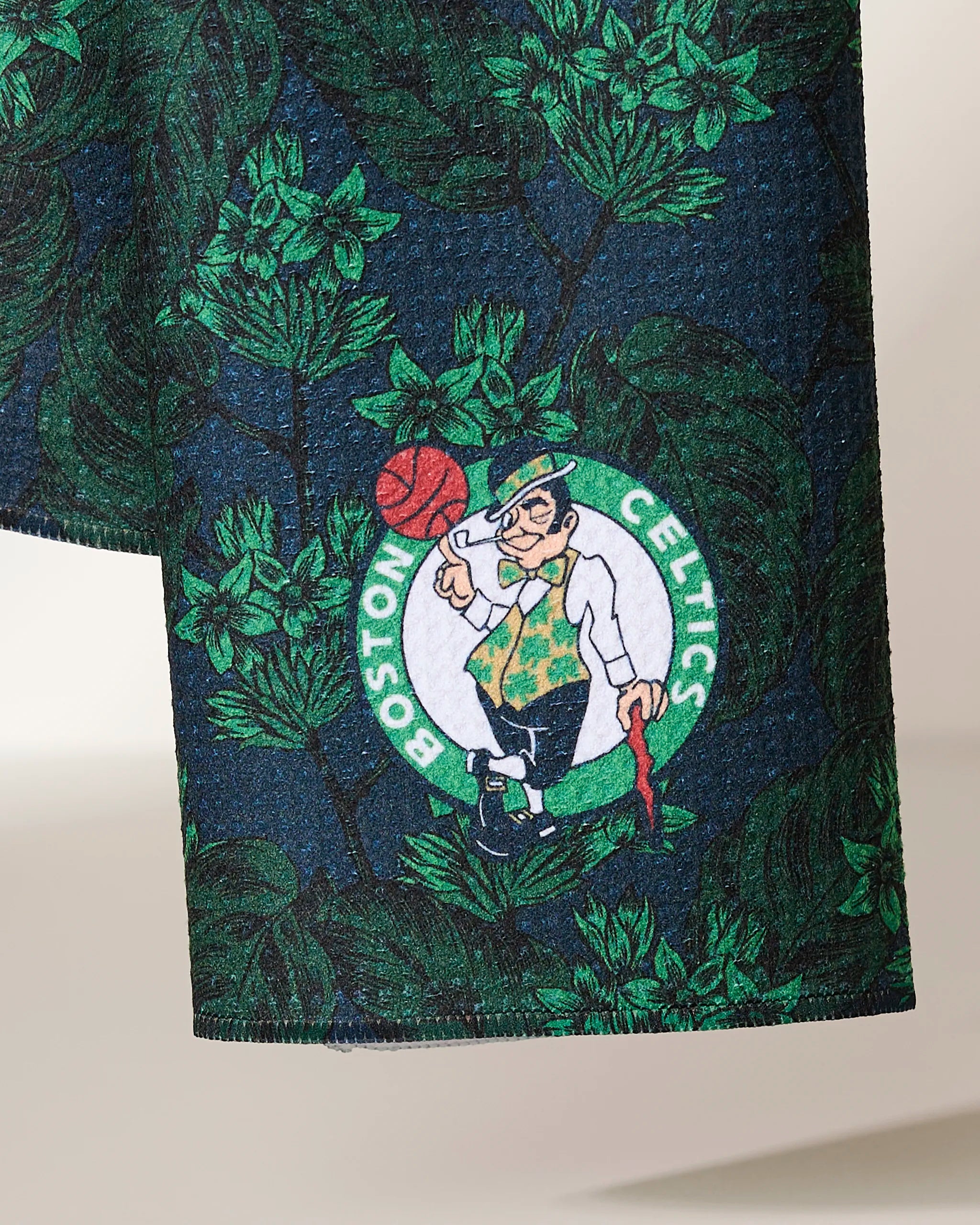 Close-up of the Celtics Floral fabric by Geometry, displaying the Boston Celtics logo—a leprechaun spinning a basketball—set among green floral patterns on a dark background.