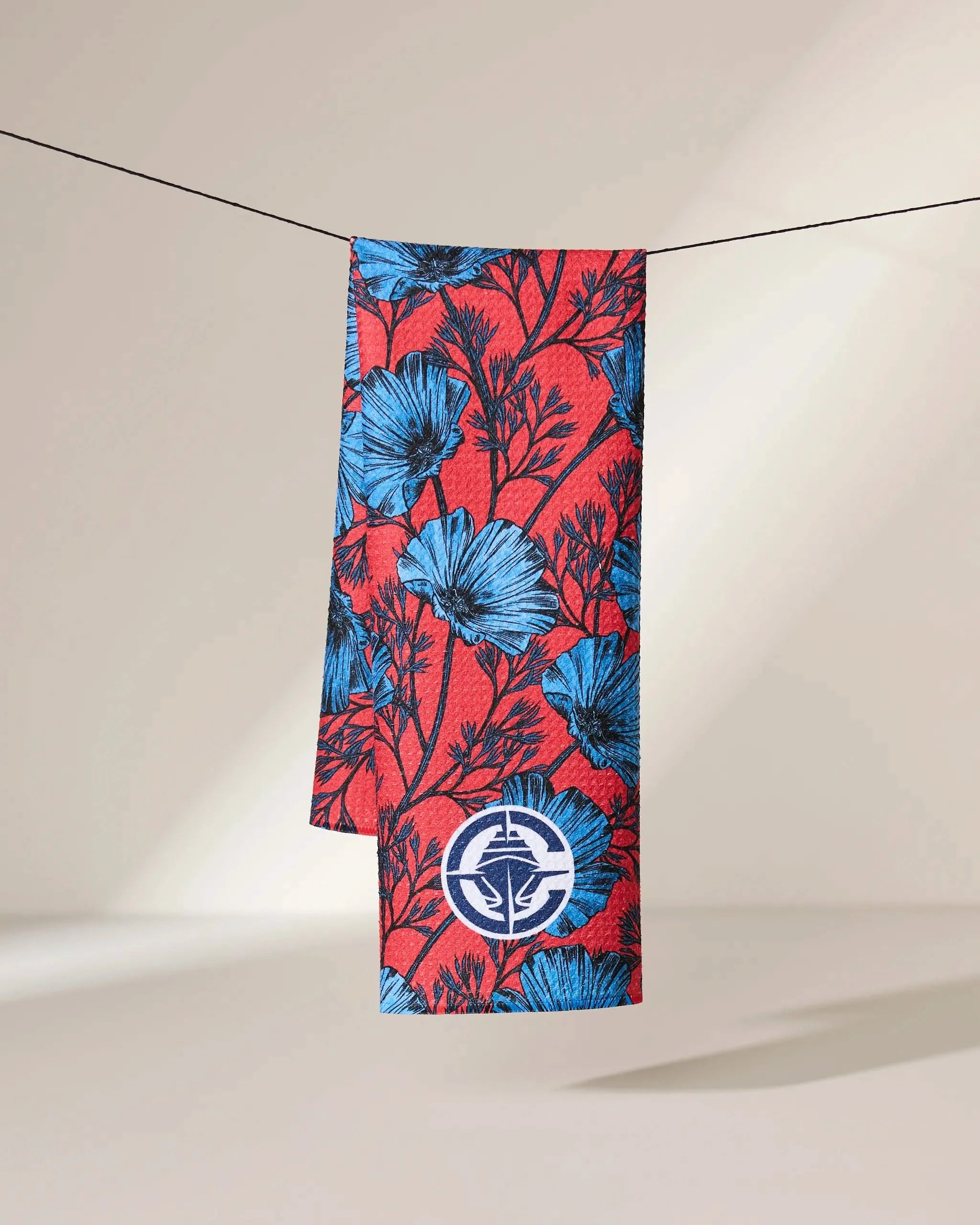 The Clippers Floral by Geometry is a rectangular fabric featuring a red background with a blue floral pattern and a white circular emblem, shown folded over a black string against a plain, light-colored backdrop.