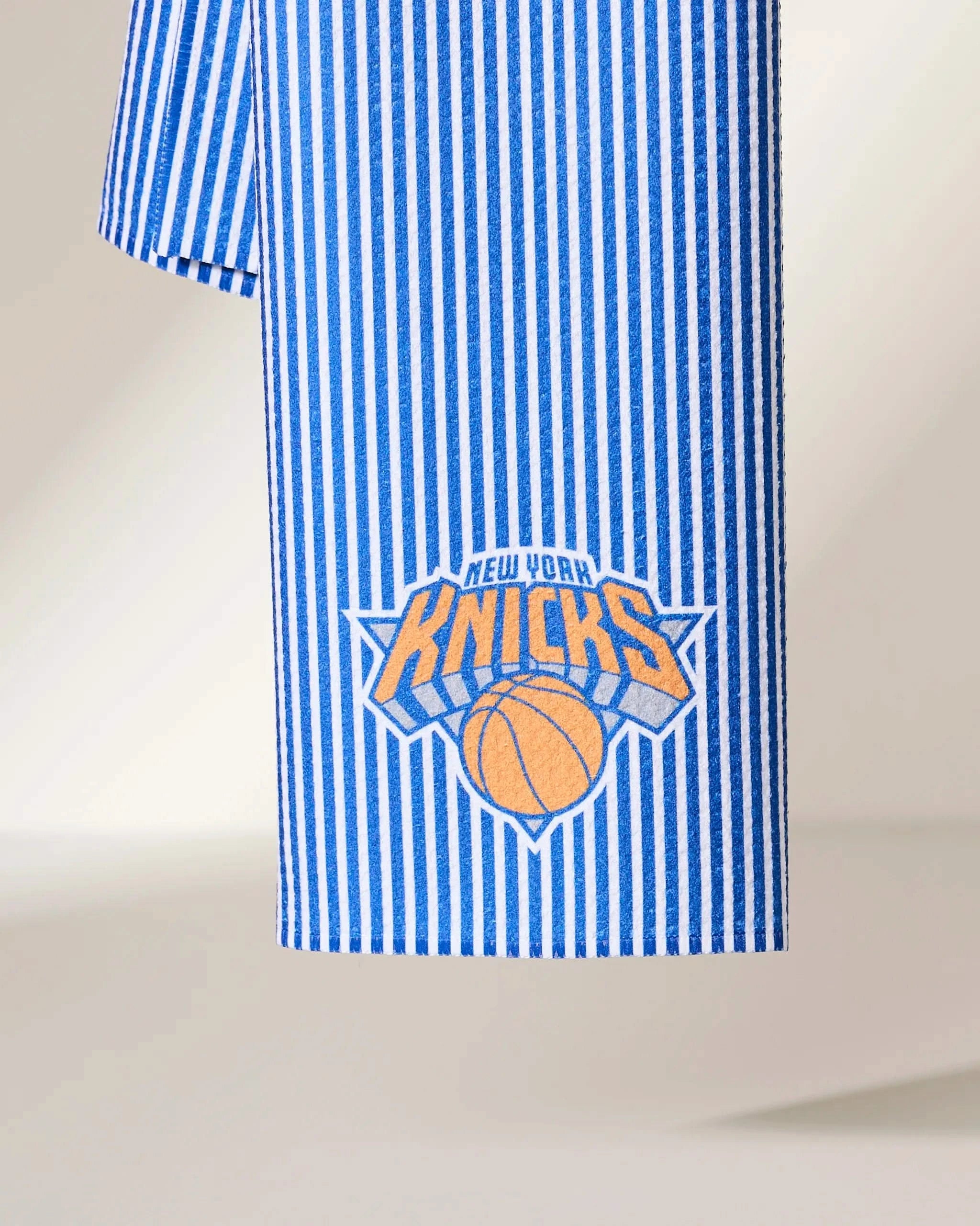 The Knicks Classic by Geometry is a blue and white vertically striped fabric with the New York Knicks logo—an orange basketball and stylized text—near the bottom edge.
