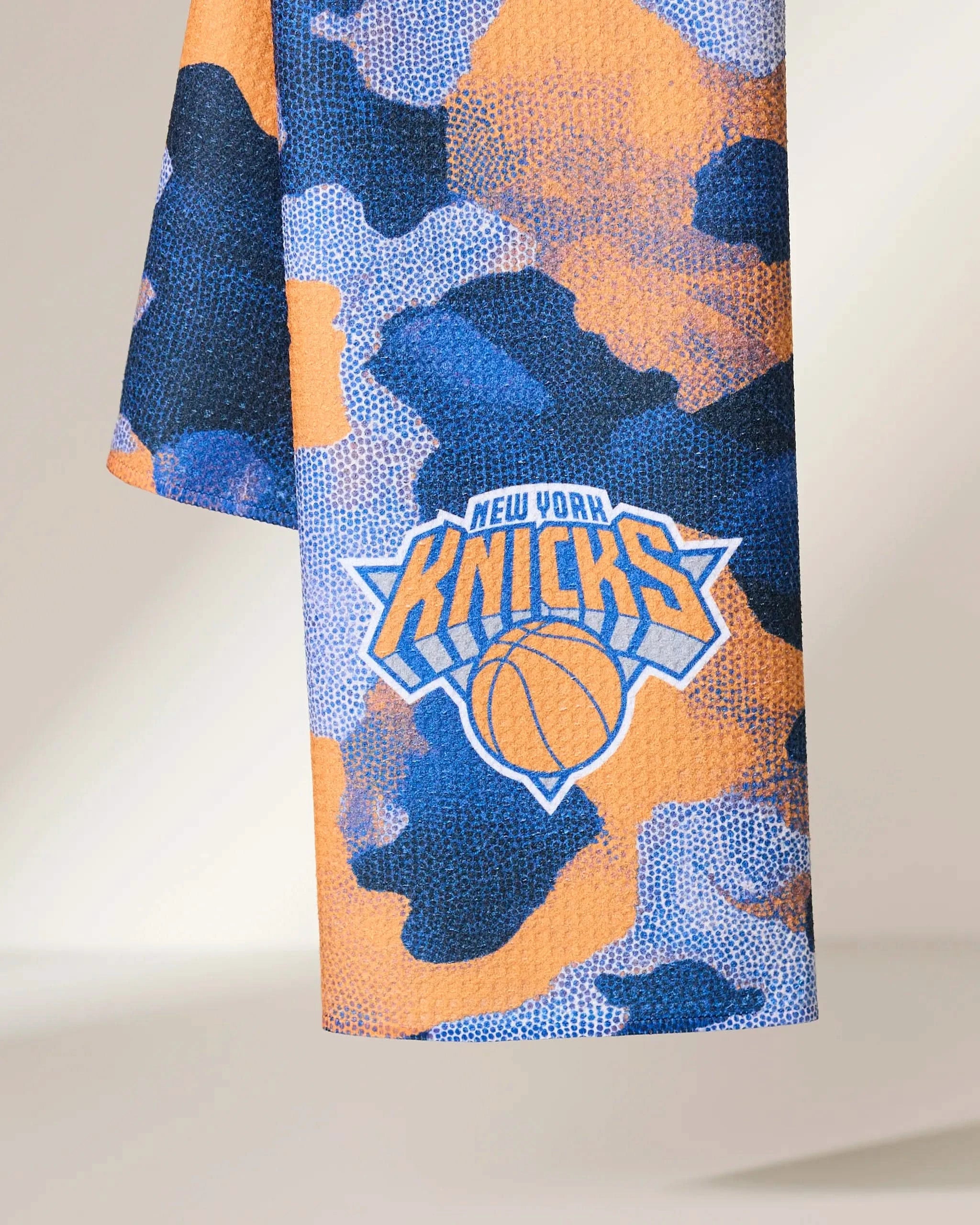 The Geometry Knicks Camo towel features a blue and orange camouflage design with the New York Knicks logo and a basketball at the center.