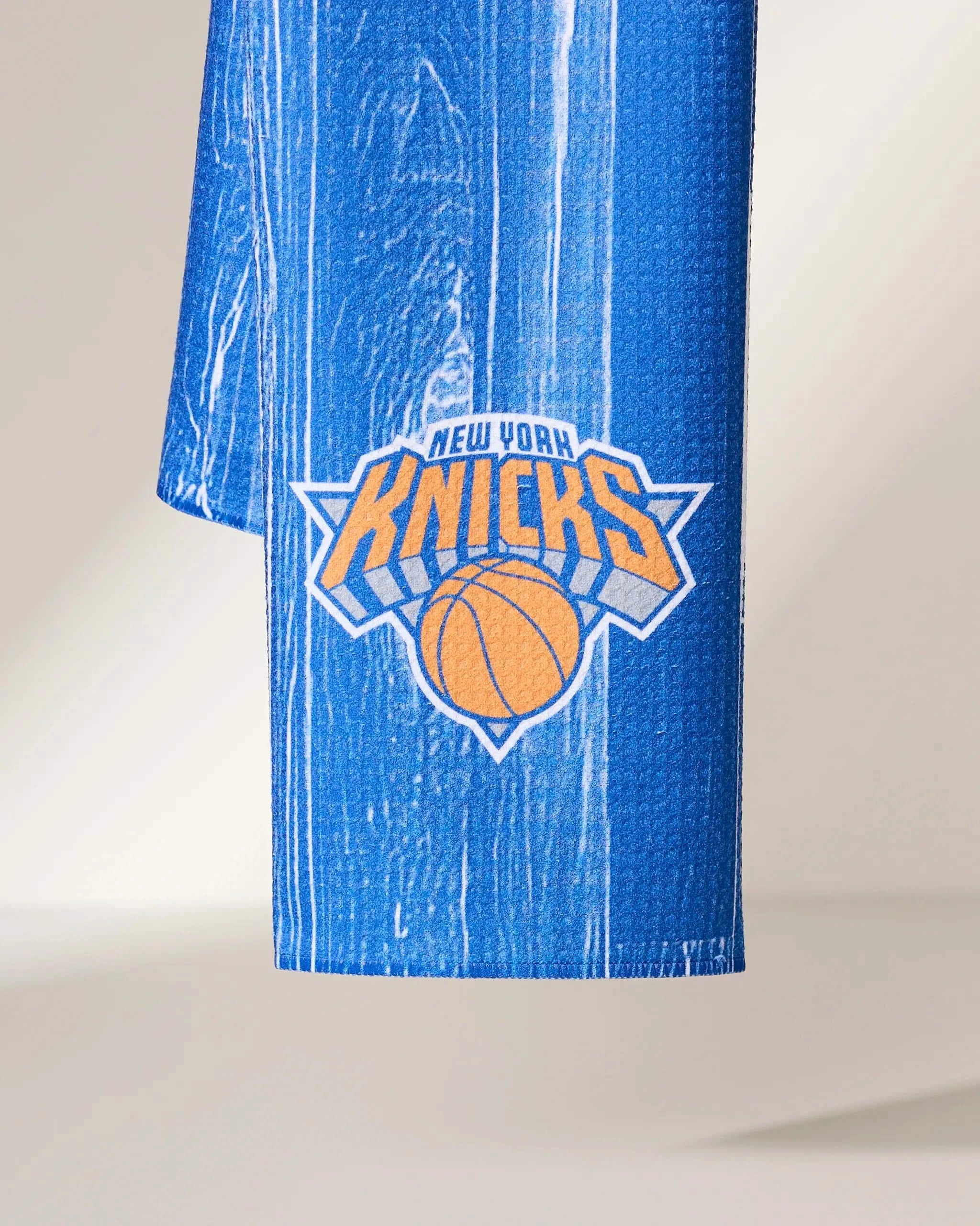 The Knicks Zone towel by Geometry is blue with a white streak pattern and features the New York Knicks logo in orange, blue, and white near the bottom.