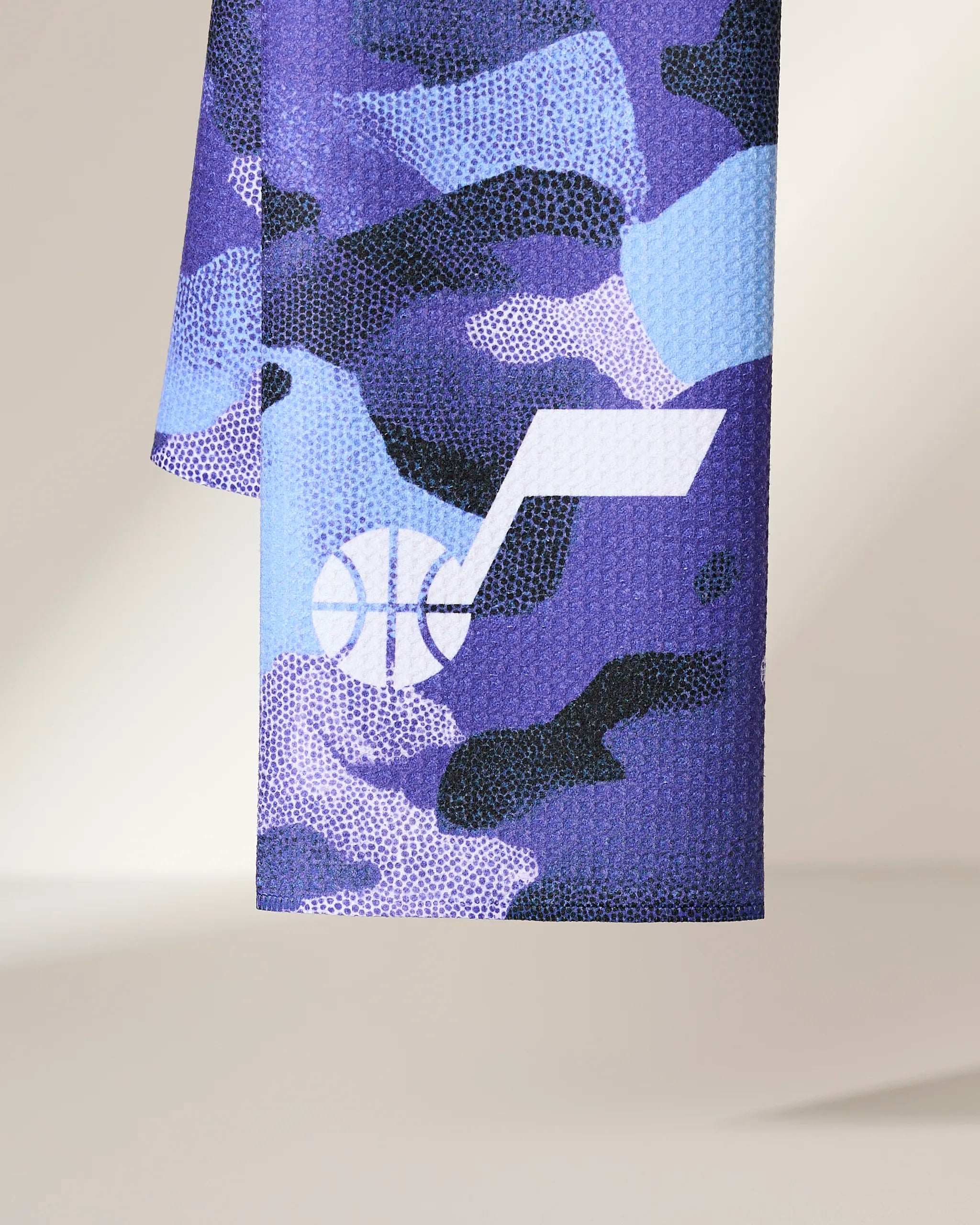 A close-up of the Jazz Camo fabric by Geometry, featuring a purple, blue, and black camouflage pattern with the white Utah Jazz basketball logo.