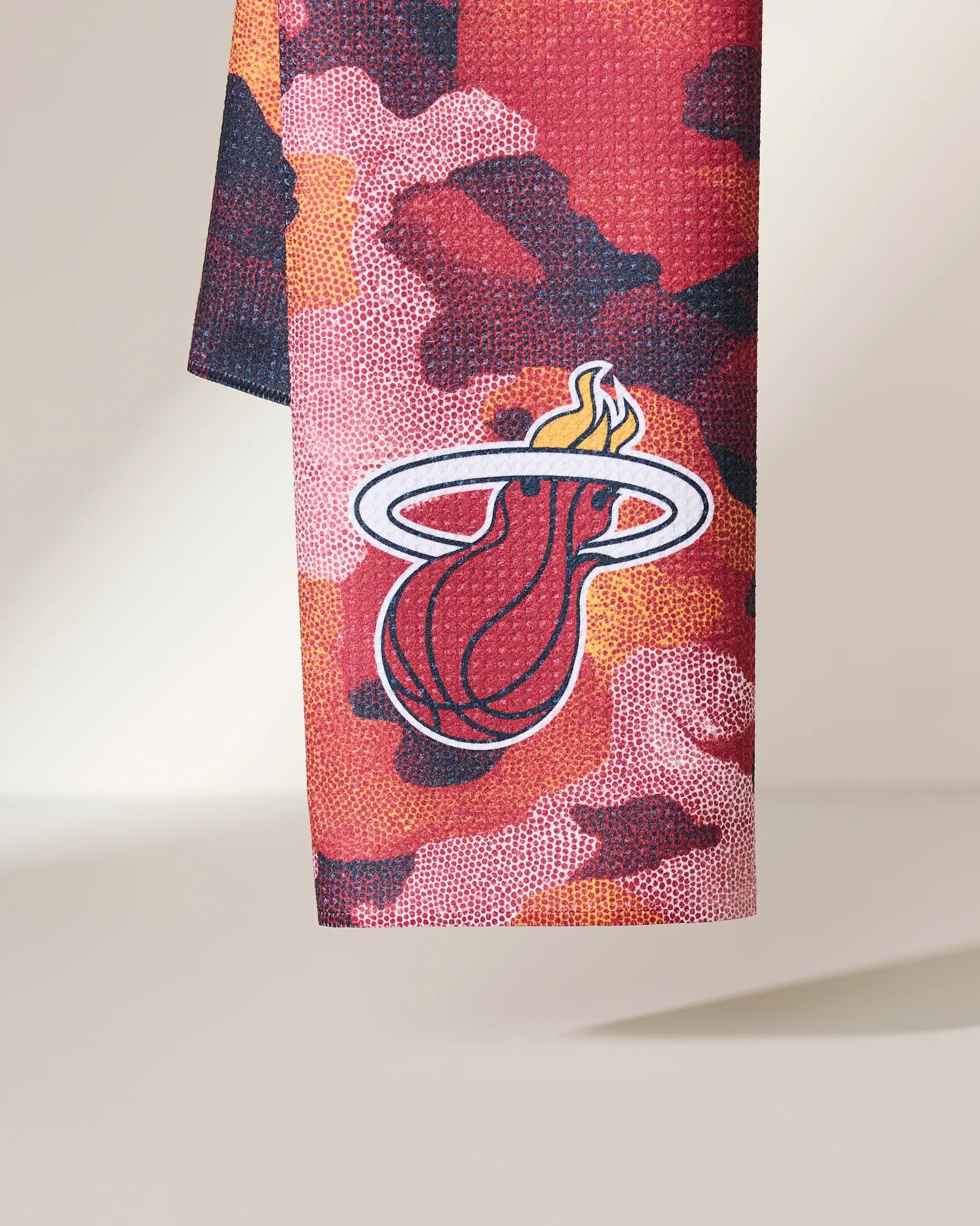 A close-up of the Geometry Heat Camo towel, showcasing a red and orange camouflage pattern with the Miami Heat logo—a flaming basketball going through a hoop.