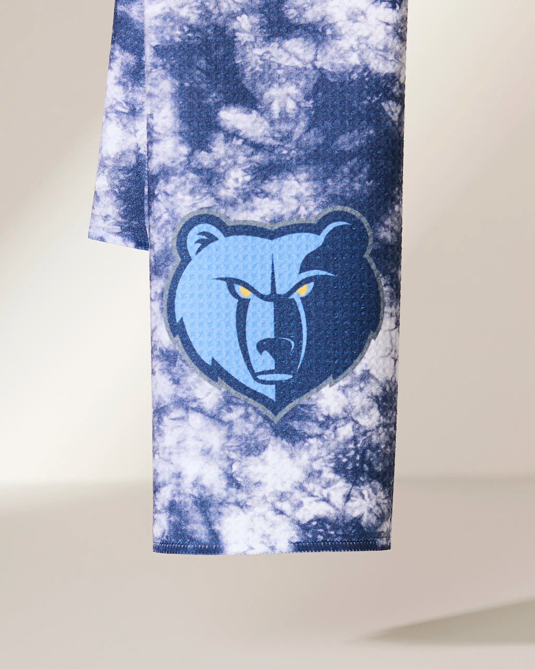 The Geometry Grizzlies Flash towel showcases a blue and white tie-dye design with the Memphis Grizzlies bear logo in blue, navy, and yellow, displayed vertically against a neutral background.