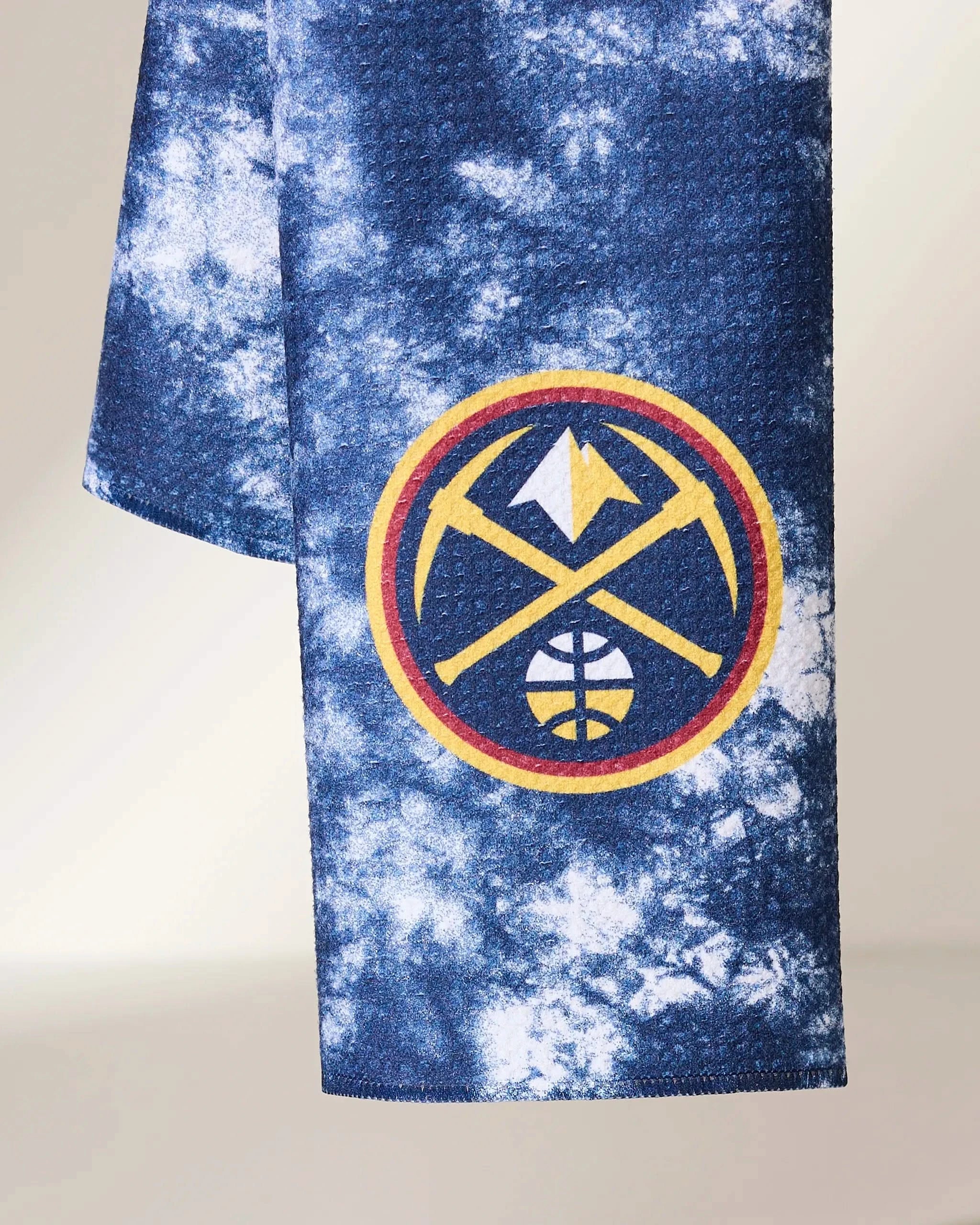 The Geometry Nuggets Flash fabric features a blue and white tie-dye design with the Denver Nuggets logo—crossed gold pickaxes, basketball, and mountain—outlined in red and yellow.