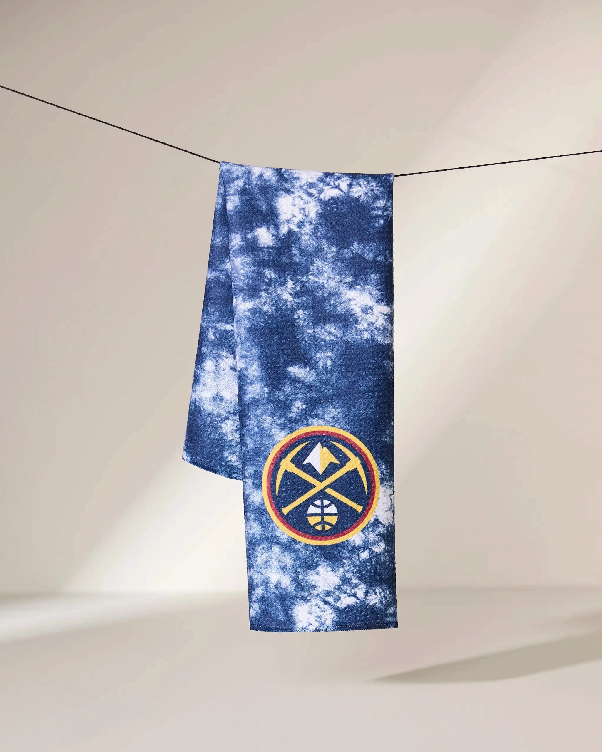 A blue and white tie-dye towel called Nuggets Flash by Geometry hangs on a line, featuring the Denver Nuggets logo in the bottom corner.
