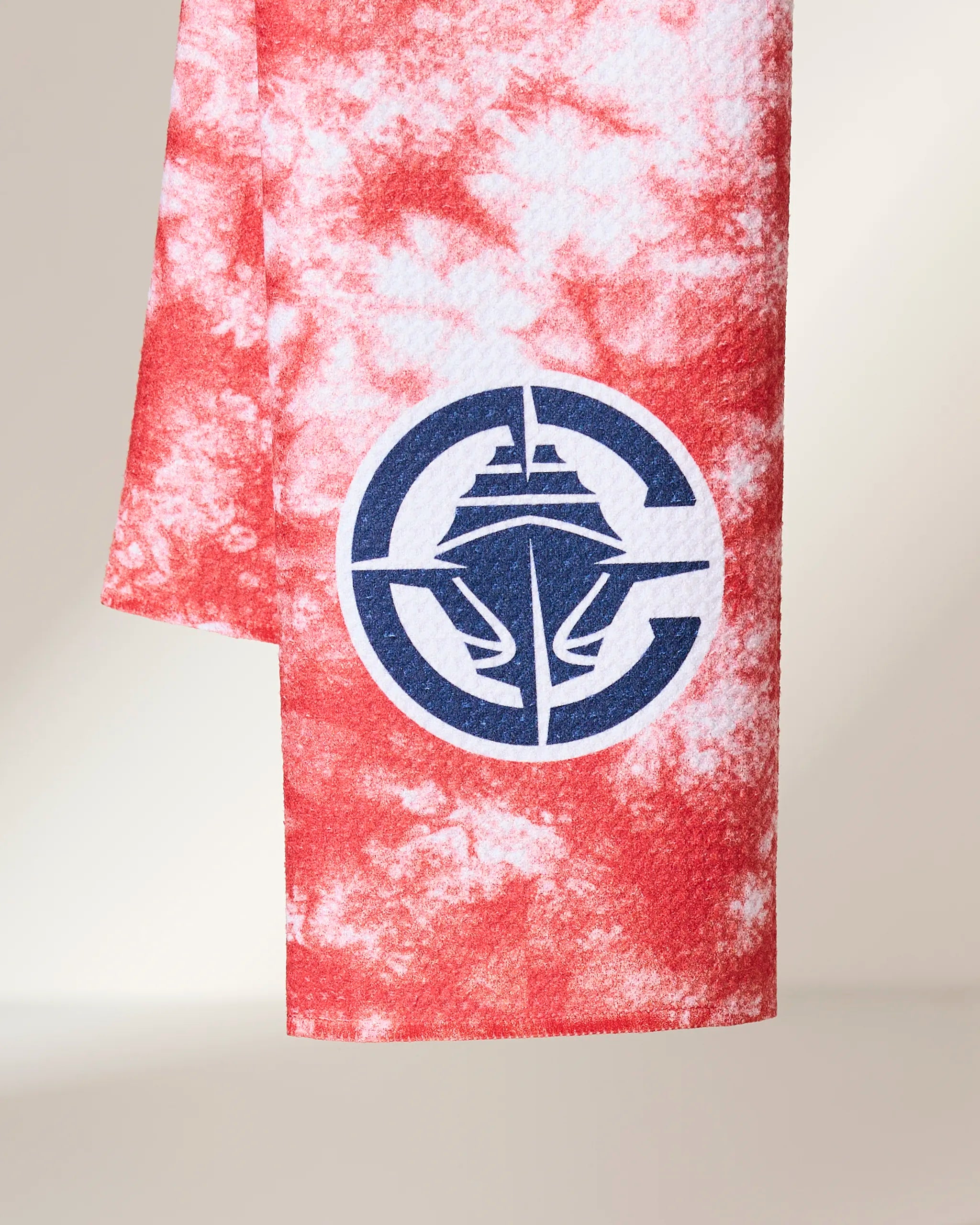 The Geometry Clipper Flash is a red and white tie-dye towel featuring a large blue circular logo with a stylized ship and anchor design at its center.