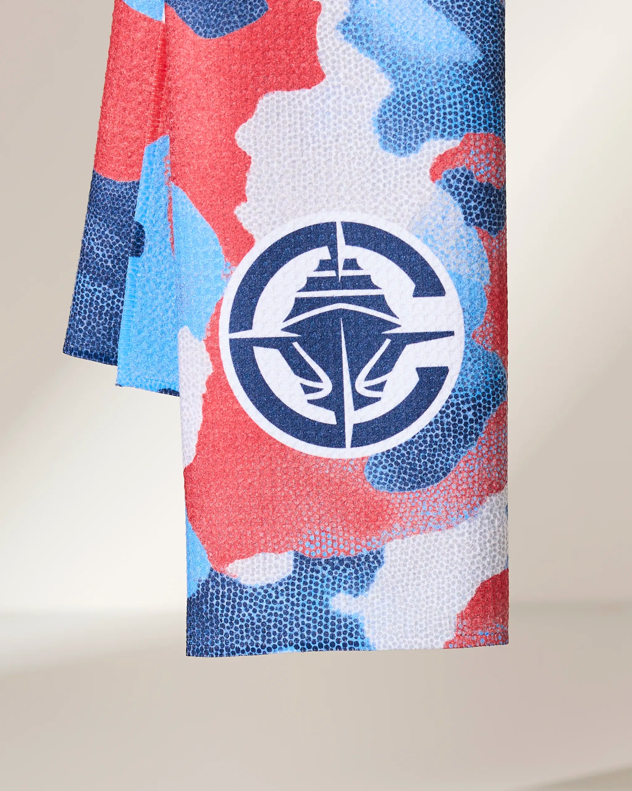 A close-up of the Geometry Clippers Camo towel, showcasing its red, blue, and white camouflage pattern and a navy circular nautical logo with a ships bow and anchor at the center.